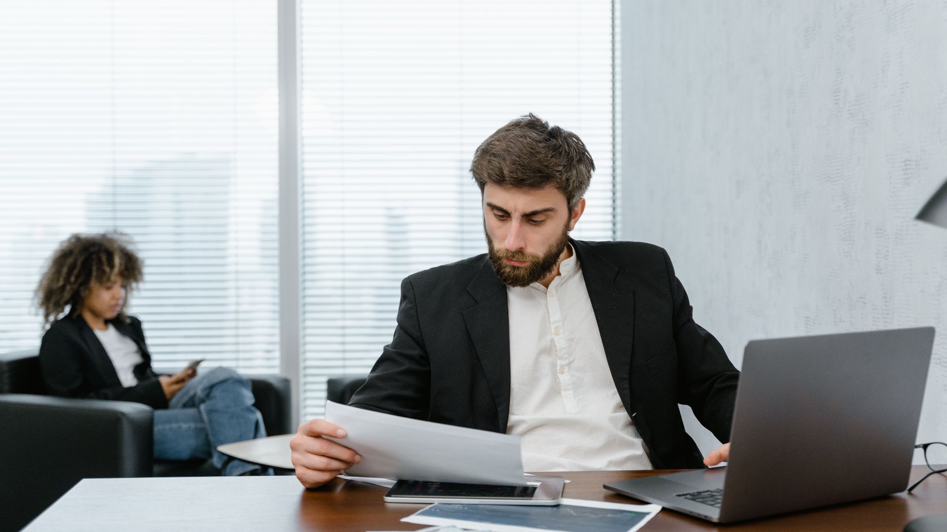 Focused businessman reviews financial reports at office desk with laptop.