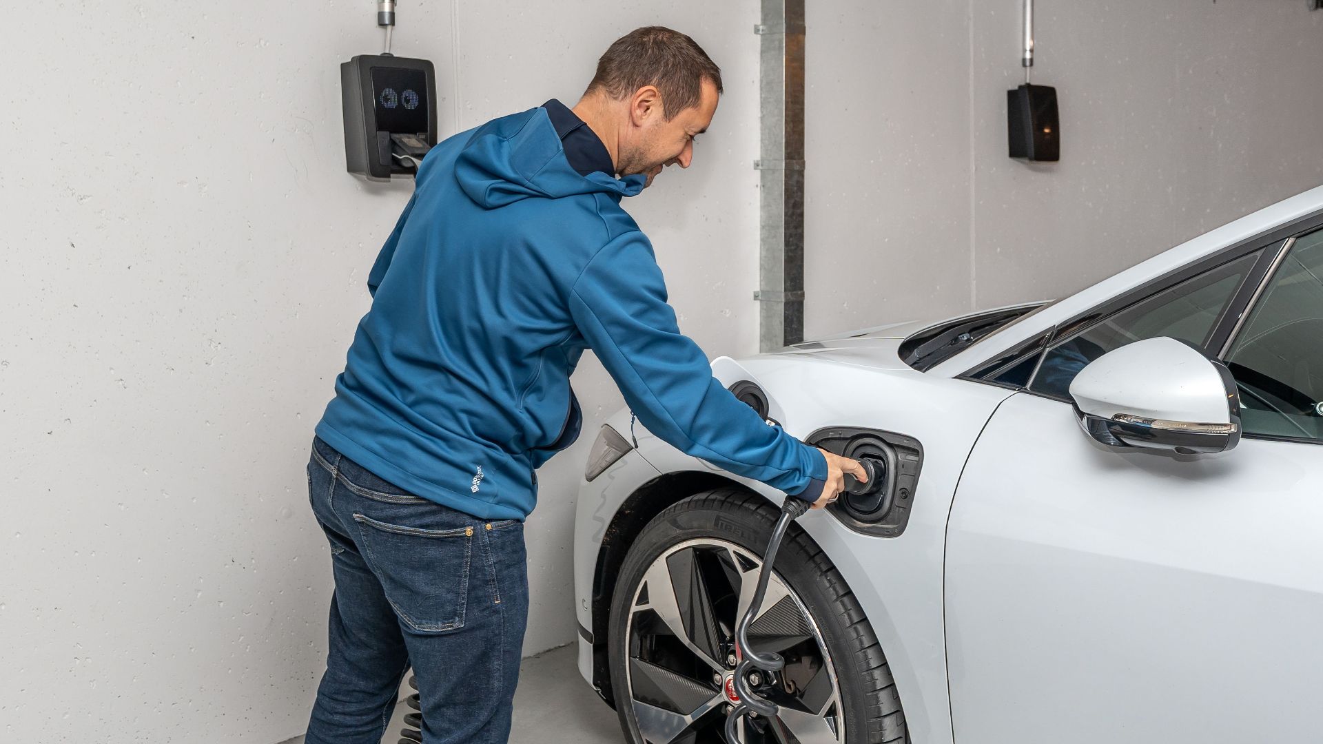 A man connects an electric car to a charging station in a modern indoor garage setting.