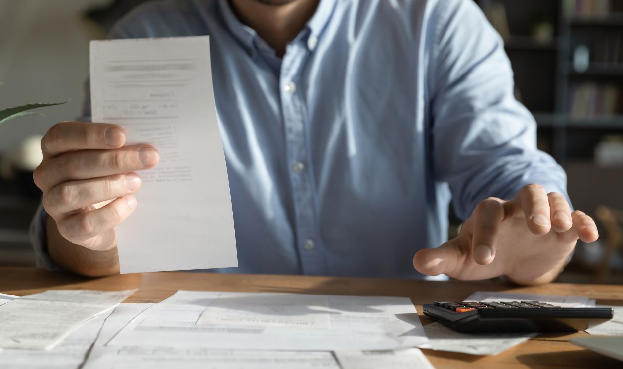 Payment check. Cropped close up young businessman do financial paperwork at office desk hold invoice receipt bill count on calculator. Paying taxes utilities reviewing expenses budgeting work concept