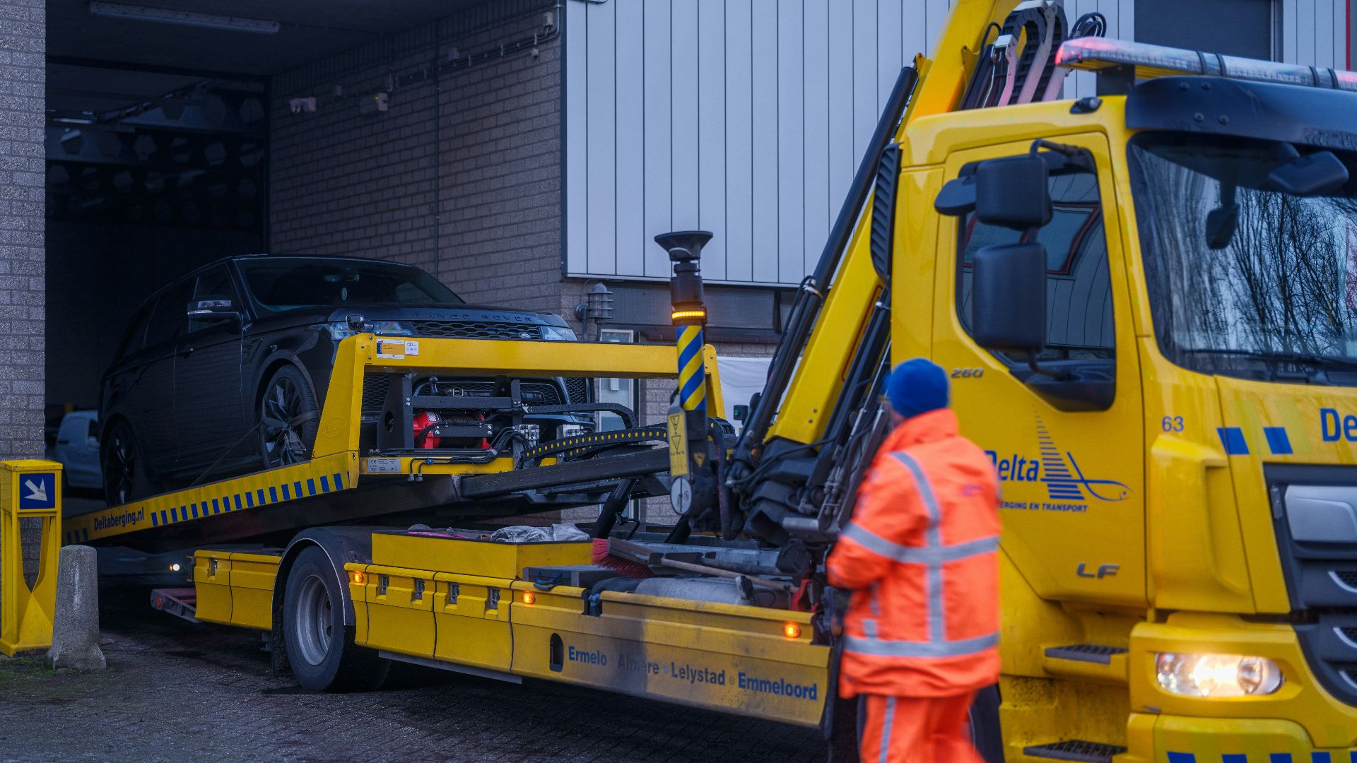 A man in an orange safety suit standing next to a yellow tow truck