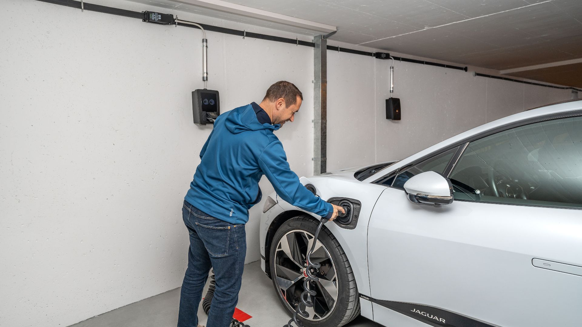 A man connects an electric car to a charging station in a modern indoor garage setting.