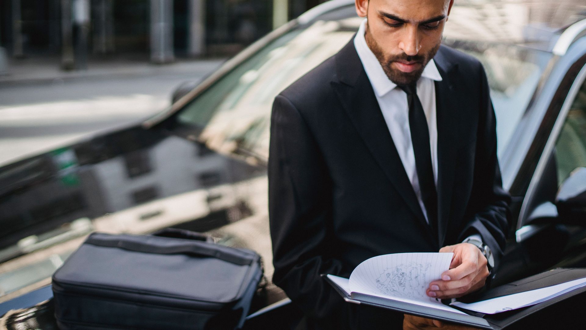Confident businessman reviewing documents on the street beside a car.