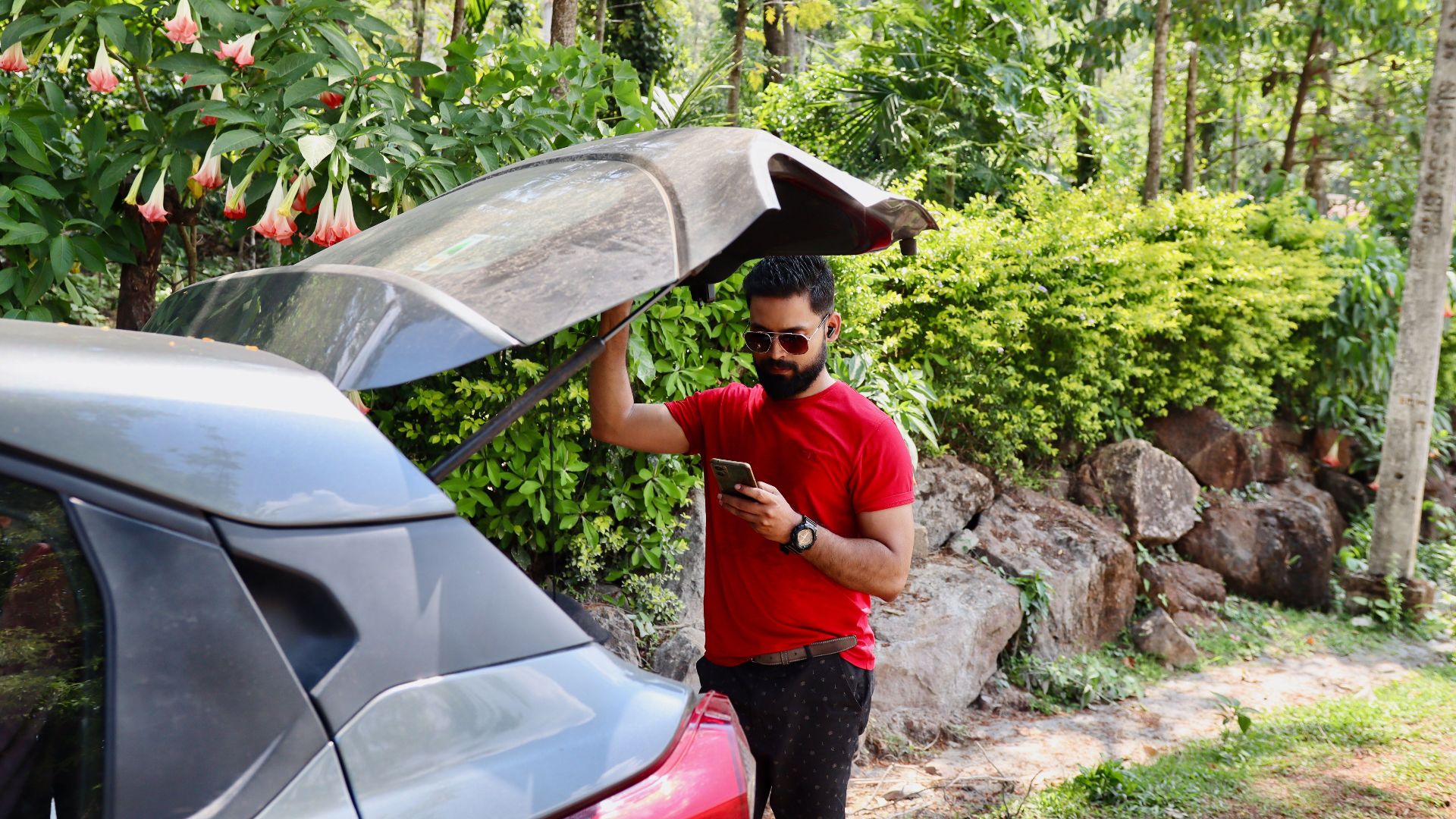 Adult man using phone near car in lush forest, Madikeri, India.