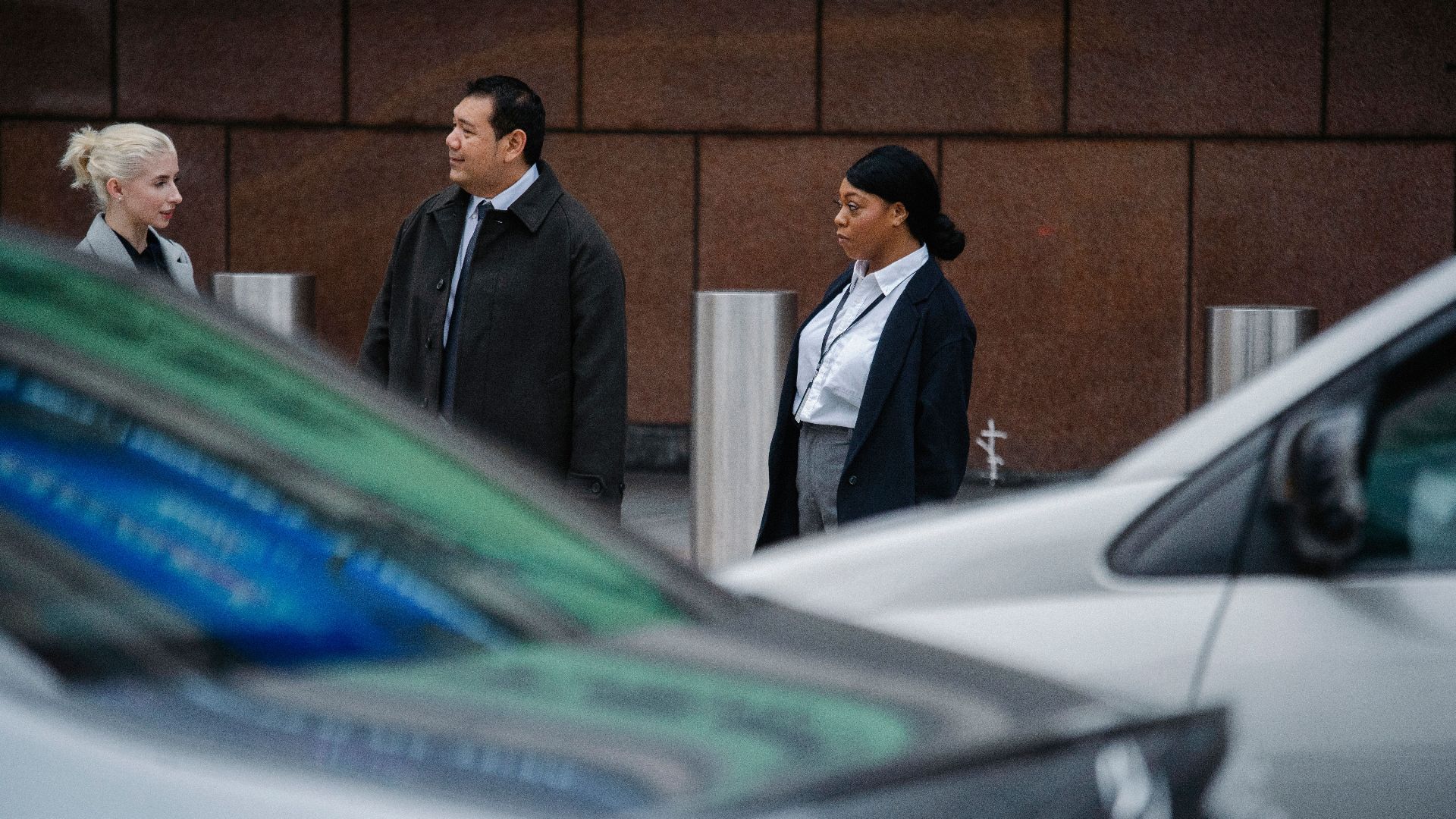 Serious multiracial coworkers wearing formal clothes standing on roadside against office building and discussing business ideas