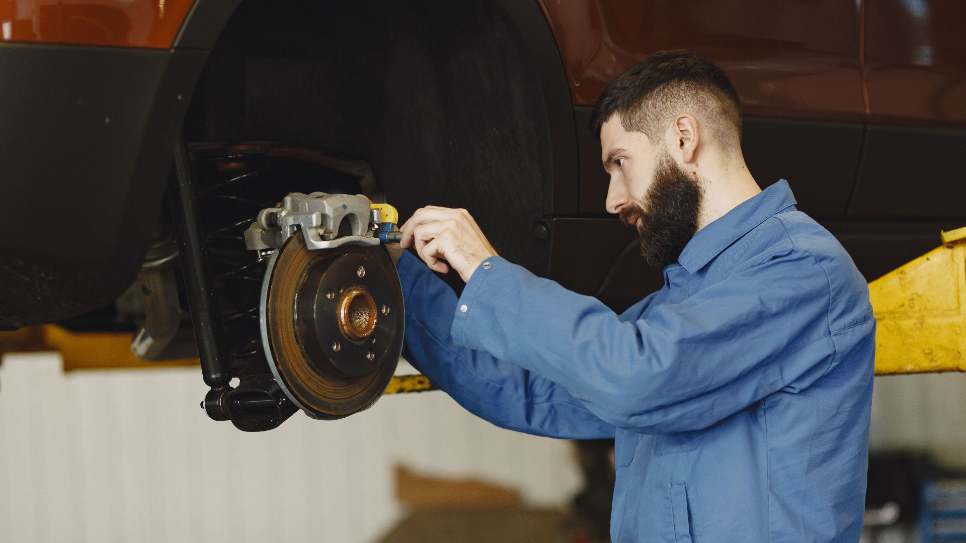 Mechanic in blue uniform performing brake repair on car in modern garage.