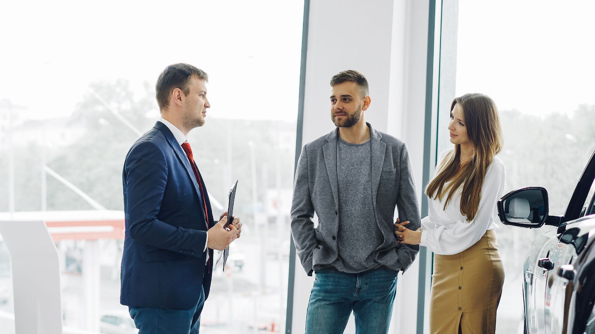 Business professional consulting a couple in a modern car dealership setting.