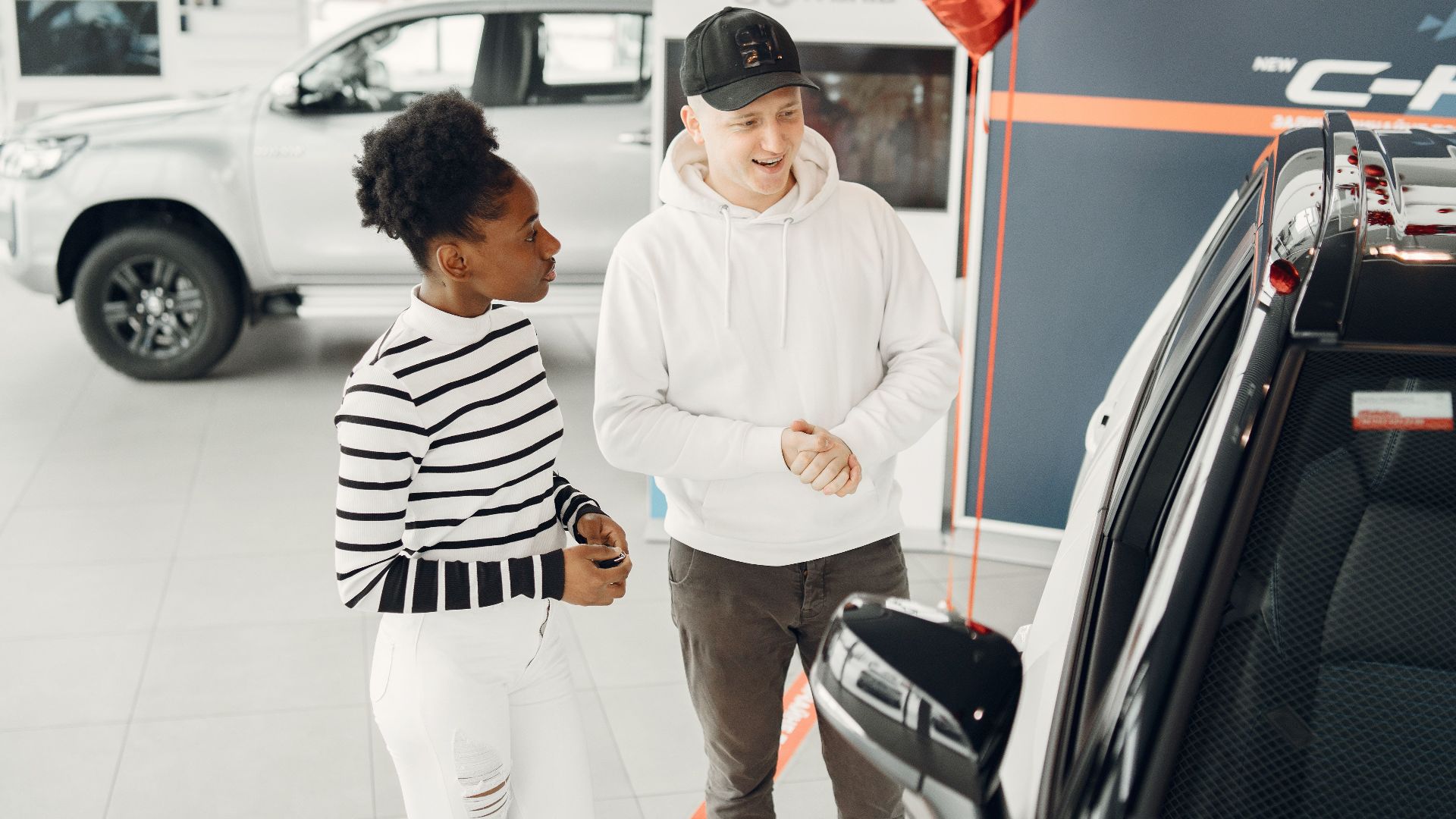 A young couple examines cars in a modern dealership showroom, highlighting customer experience.