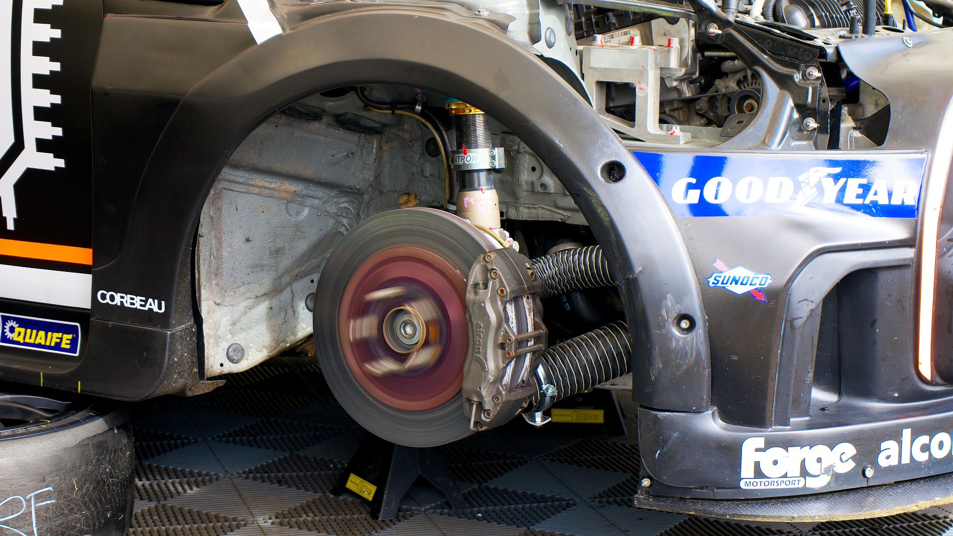 Close-up of race car undergoing maintenance in Silverstone, showing disc brake and tools.