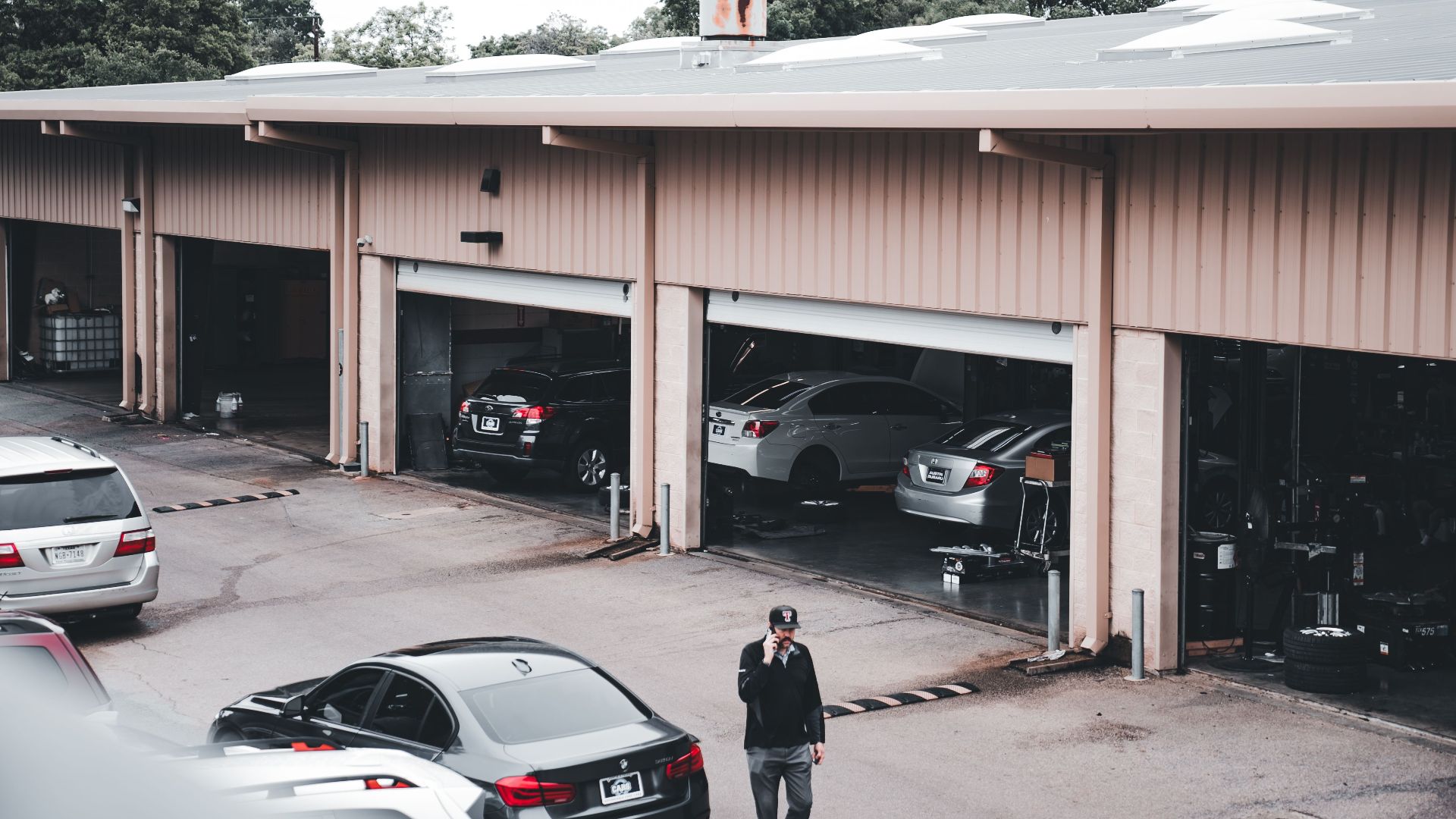A man walks by a garage with cars parked inside and outside in an urban setting.