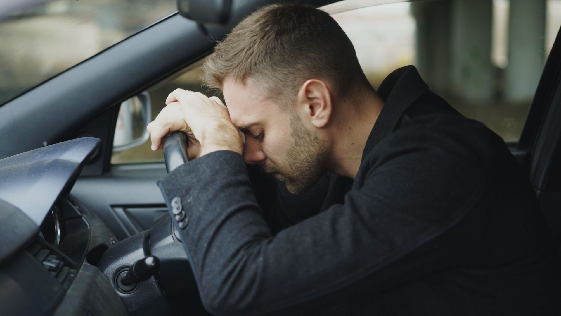 A man showing stress while sitting in a car, head on steering wheel.