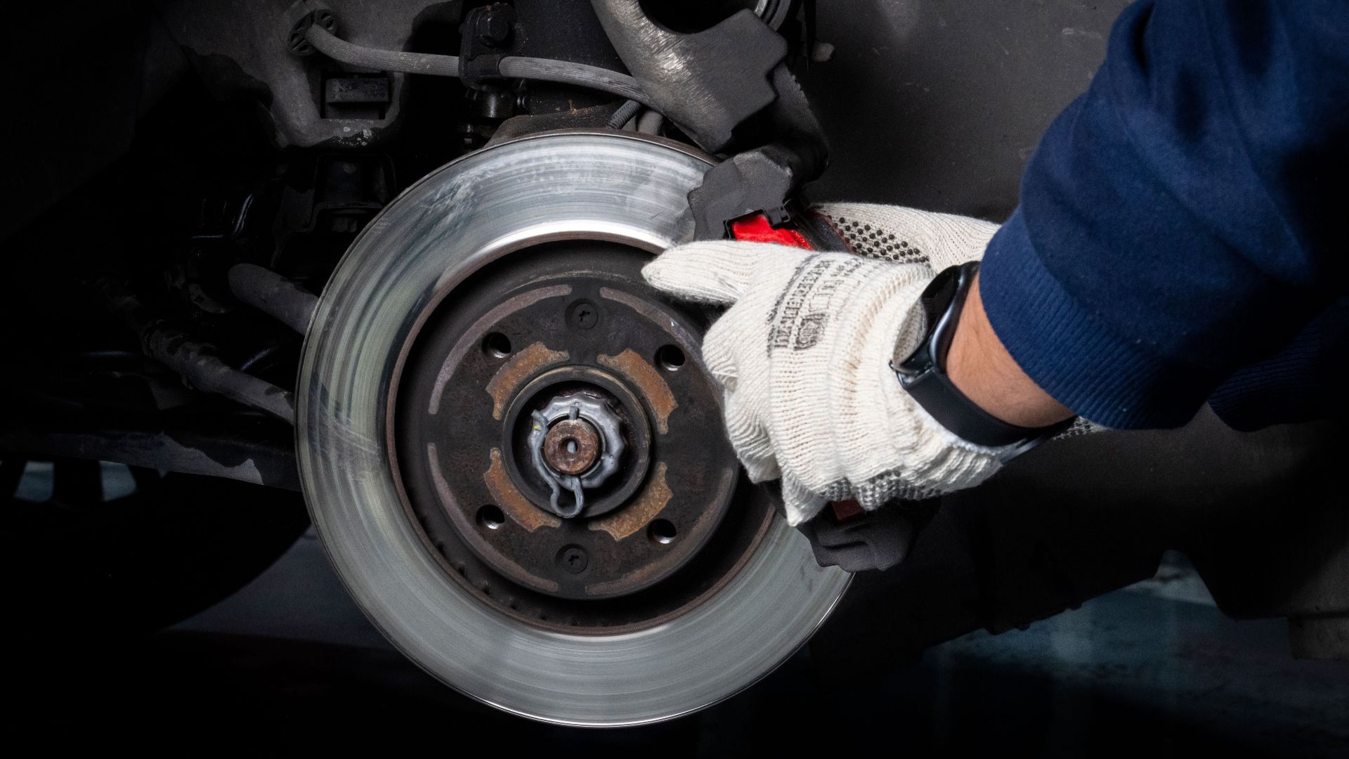 Mechanic working on car brake system in a workshop setting.