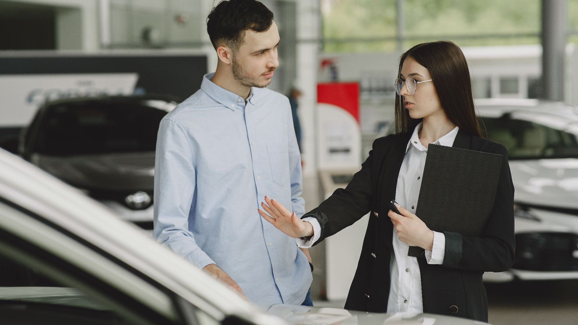 A salesperson and customer discussing car features in a dealership setting.