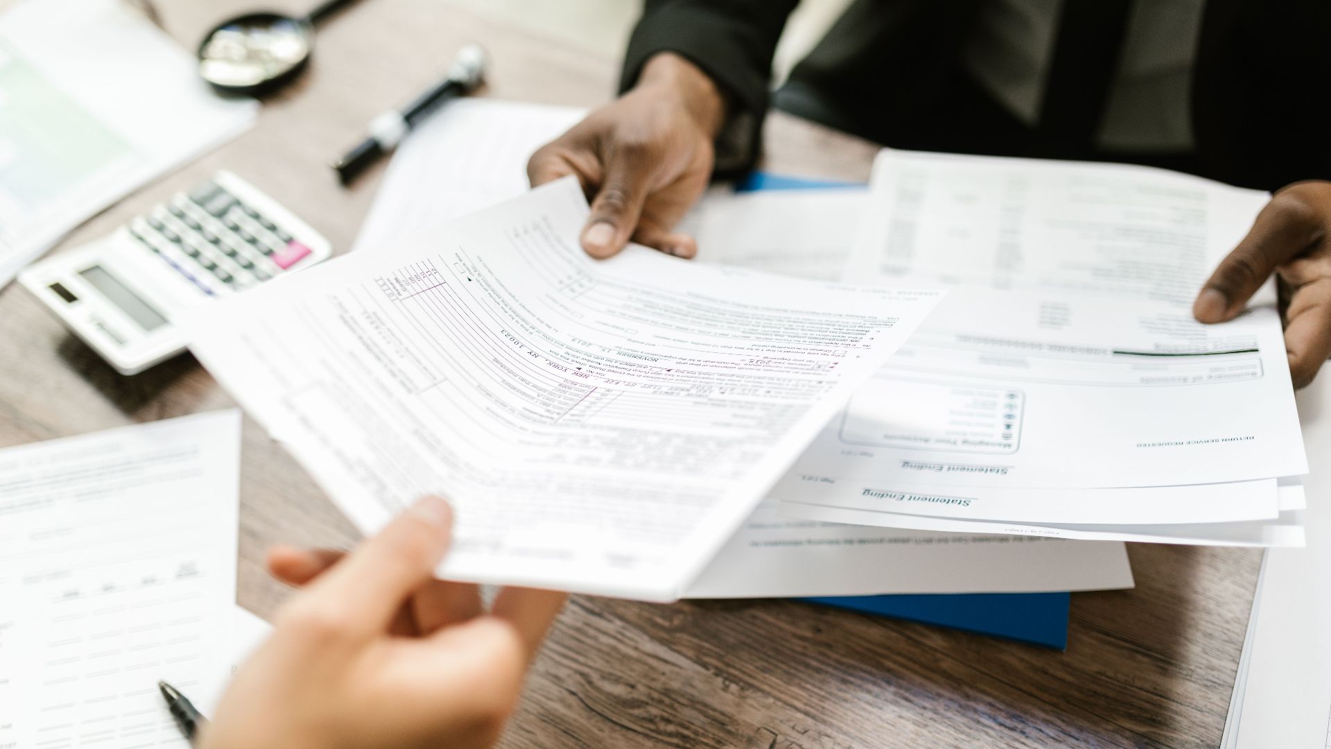 Two professionals exchanging documents in an office setting, focusing on paperwork and data analysis.