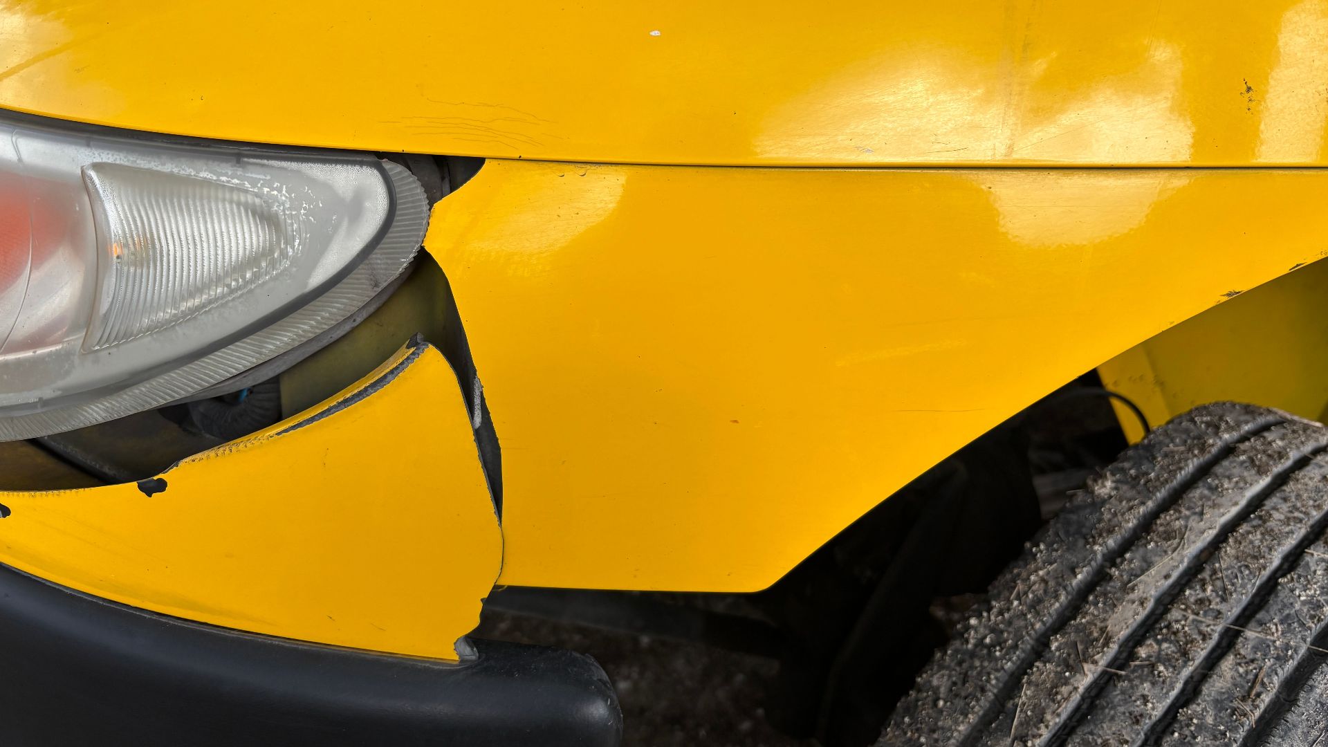 Close-up image of a yellow car's damaged front bumper and headlight for insurance or accident concept.