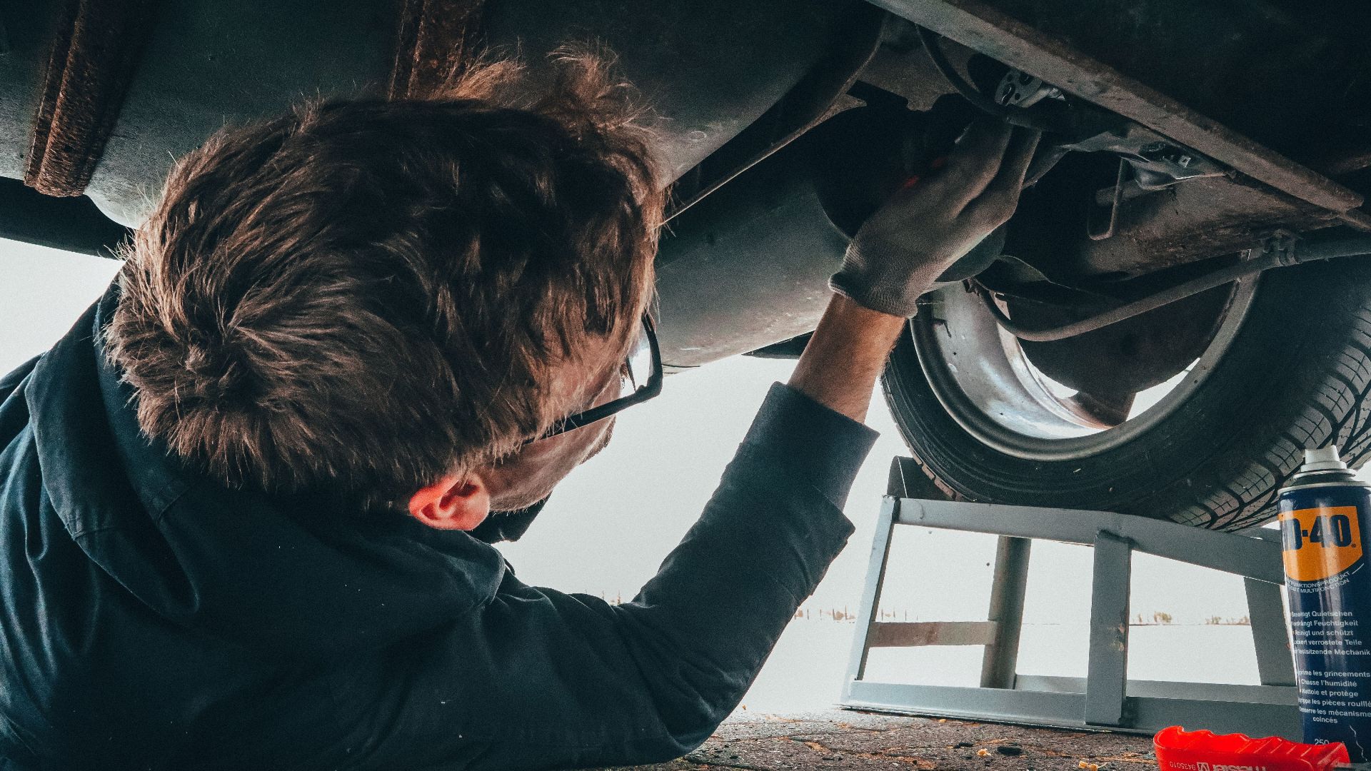 Mechanic skillfully repairing car undercarriage in outdoor setting with tools.