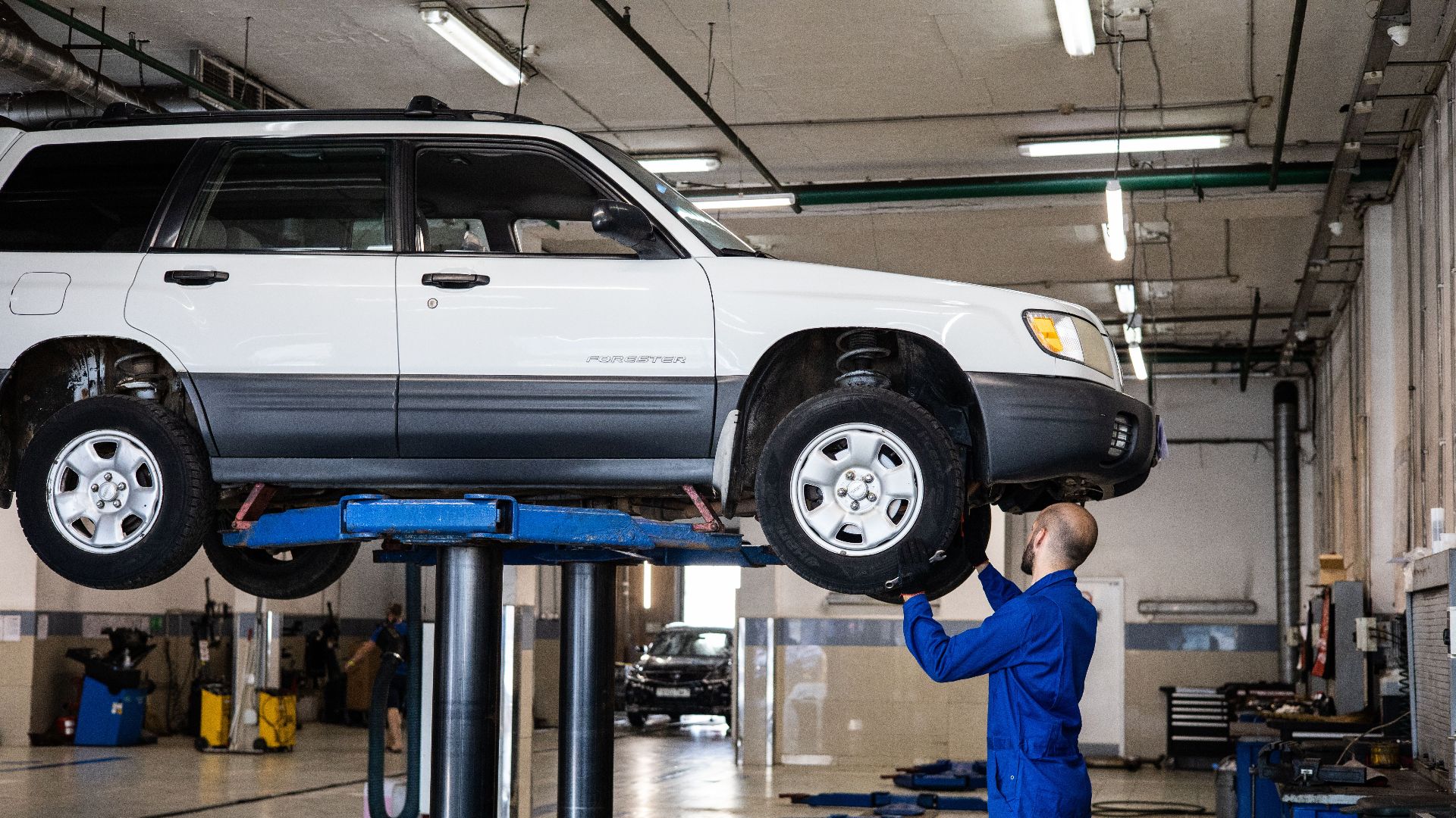 A mechanic inspecting a white SUV lifted in a well-lit auto repair shop.
