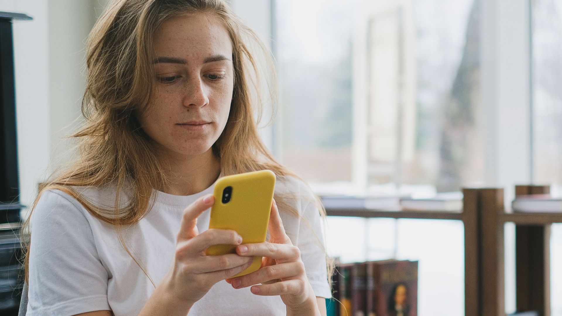 Young woman multitasking with smartphone and laptop in a cozy indoor setting.