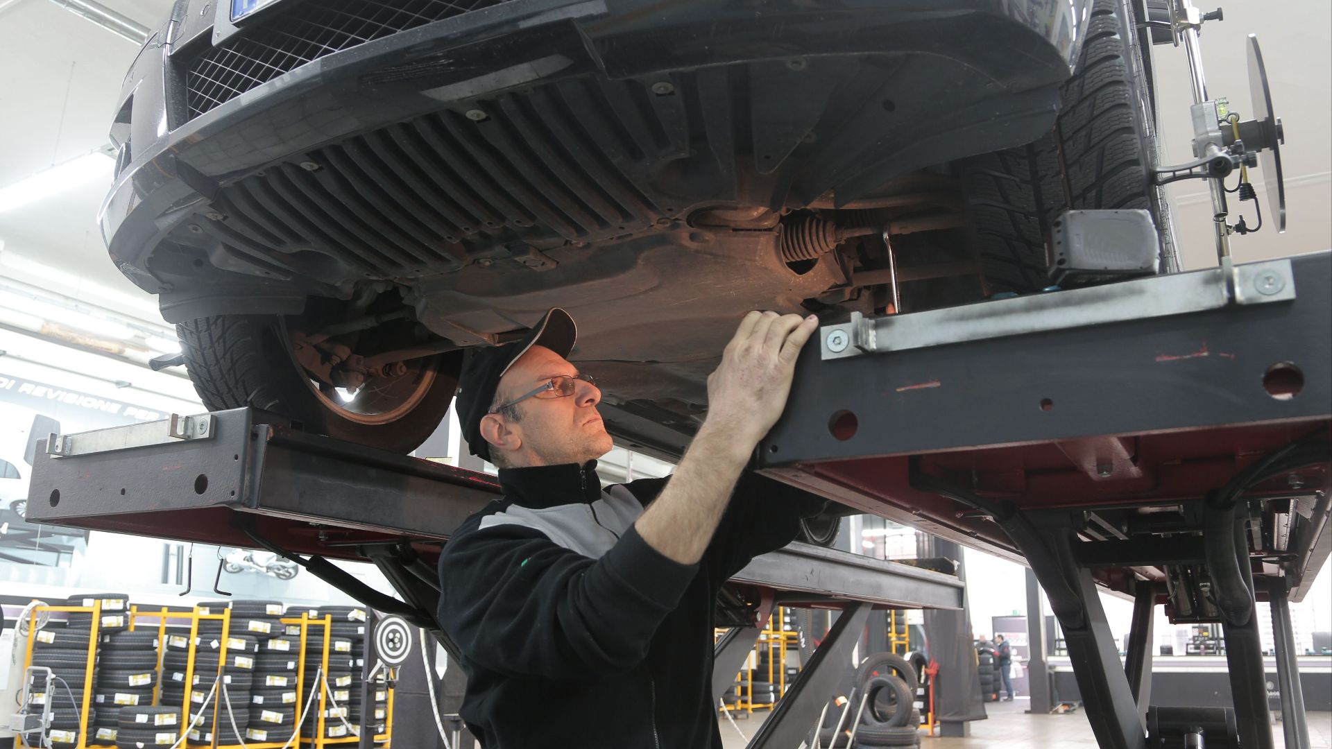Mechanic inspecting car on lift in an automotive garage, focusing on vehicle repair and maintenance.