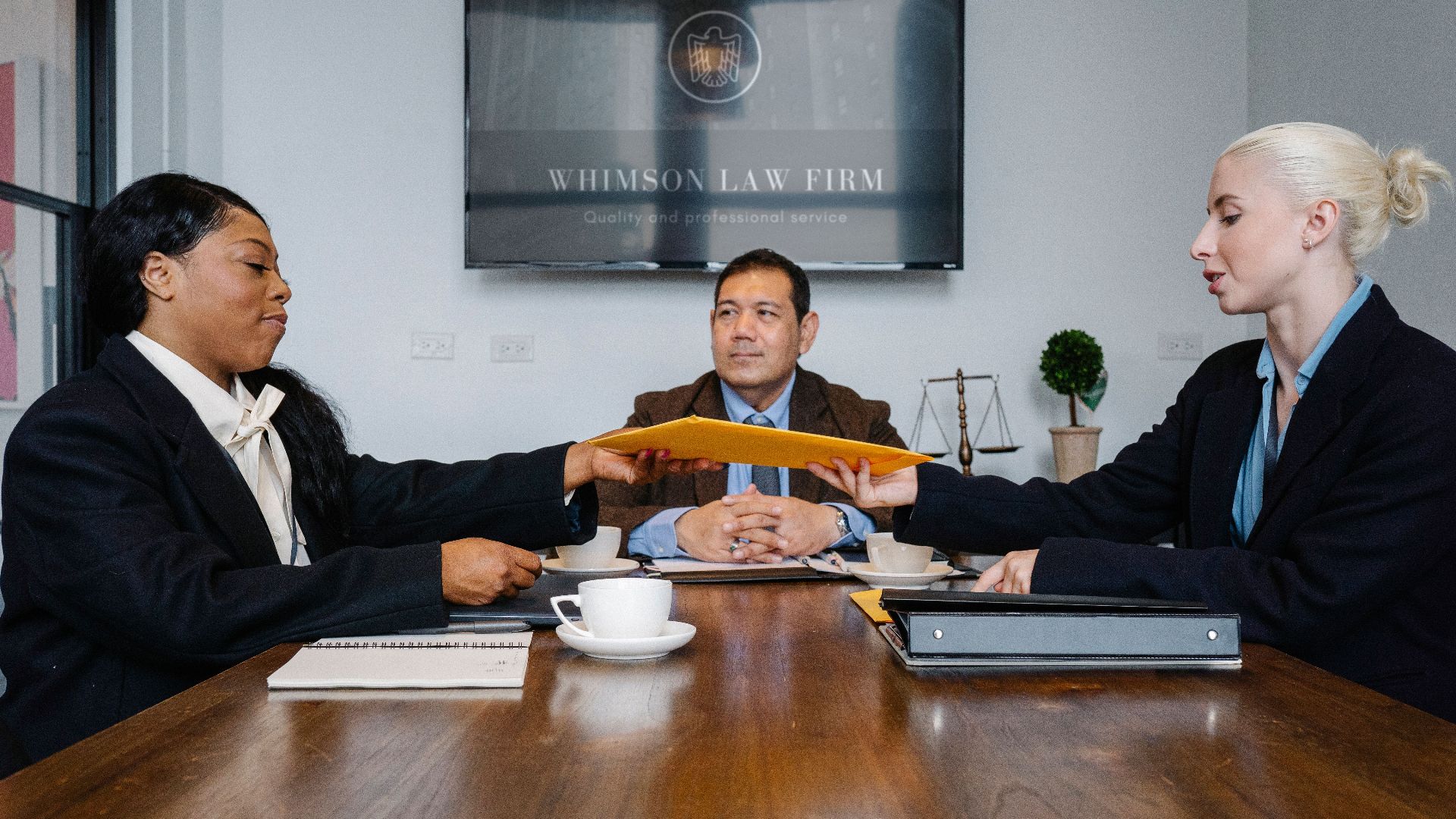 Group of cheerful diverse colleagues discussing court decision at table with notepad and cup