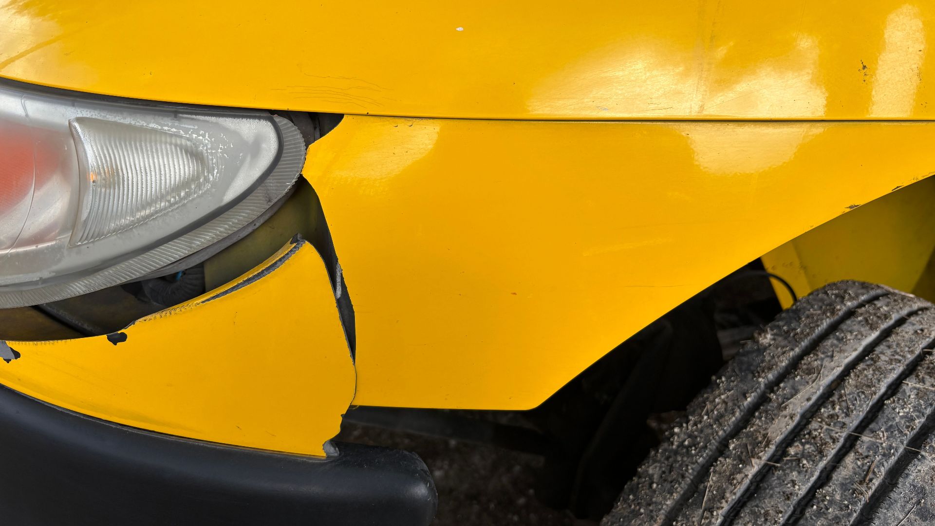 Close-up image of a yellow car's damaged front bumper and headlight for insurance or accident concept.