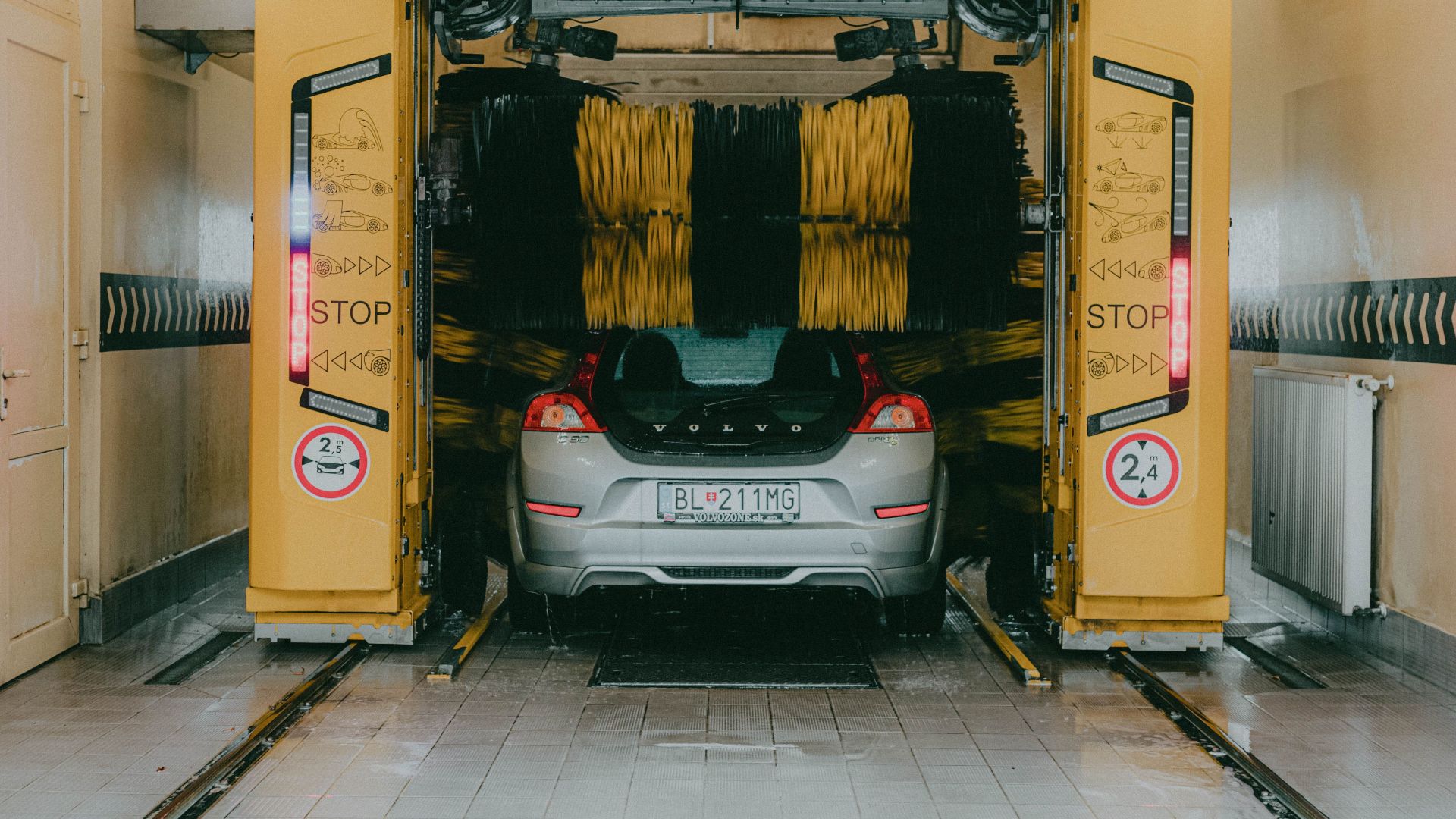 A car undergoing a cleaning process in an automated car wash station with a yellow gantry machine.