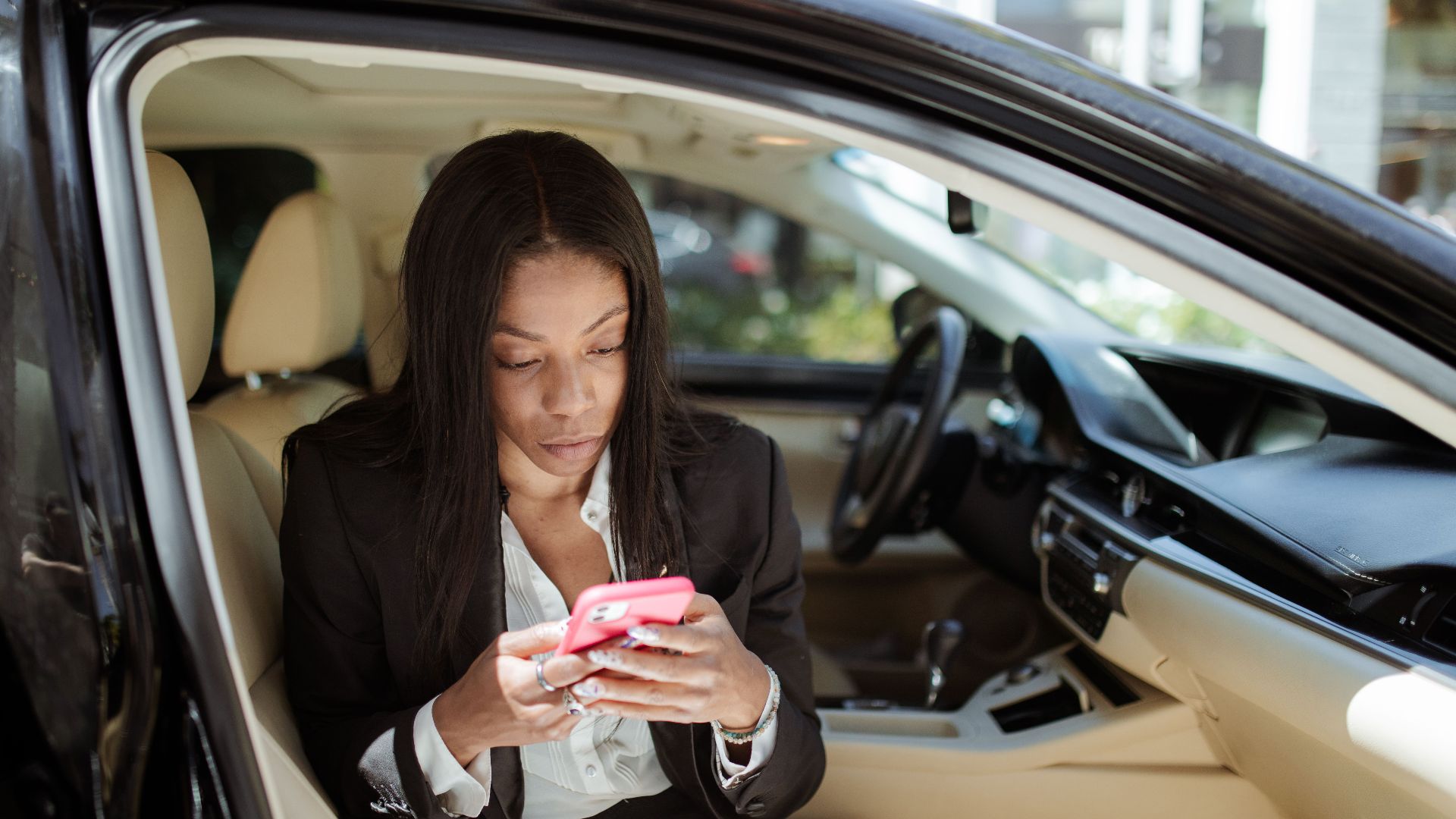 A businesswoman uses her smartphone while seated in a car, focusing intently on the screen.