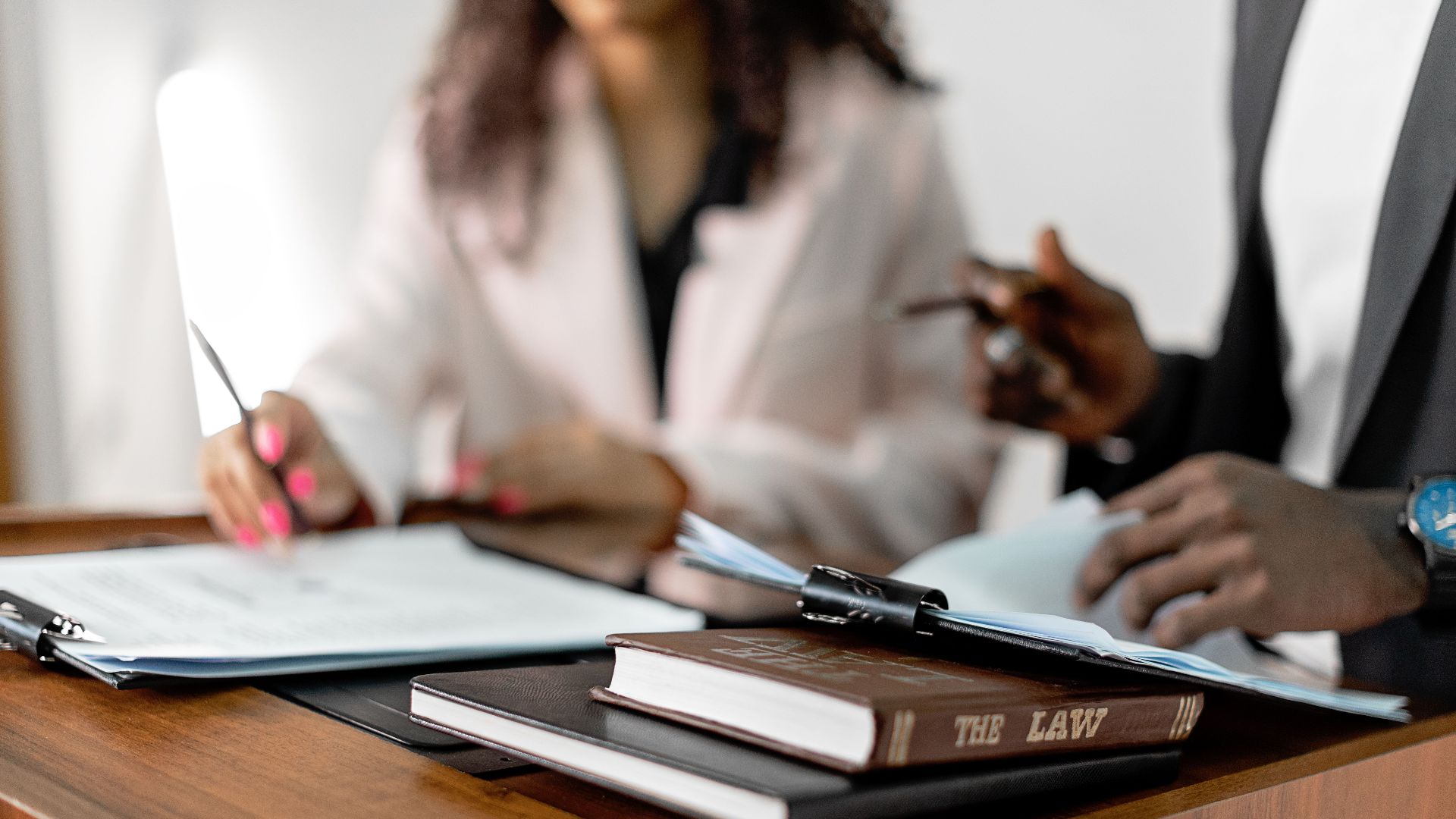 Two lawyers reviewing documents with law books on a desk. Professional legal environment.