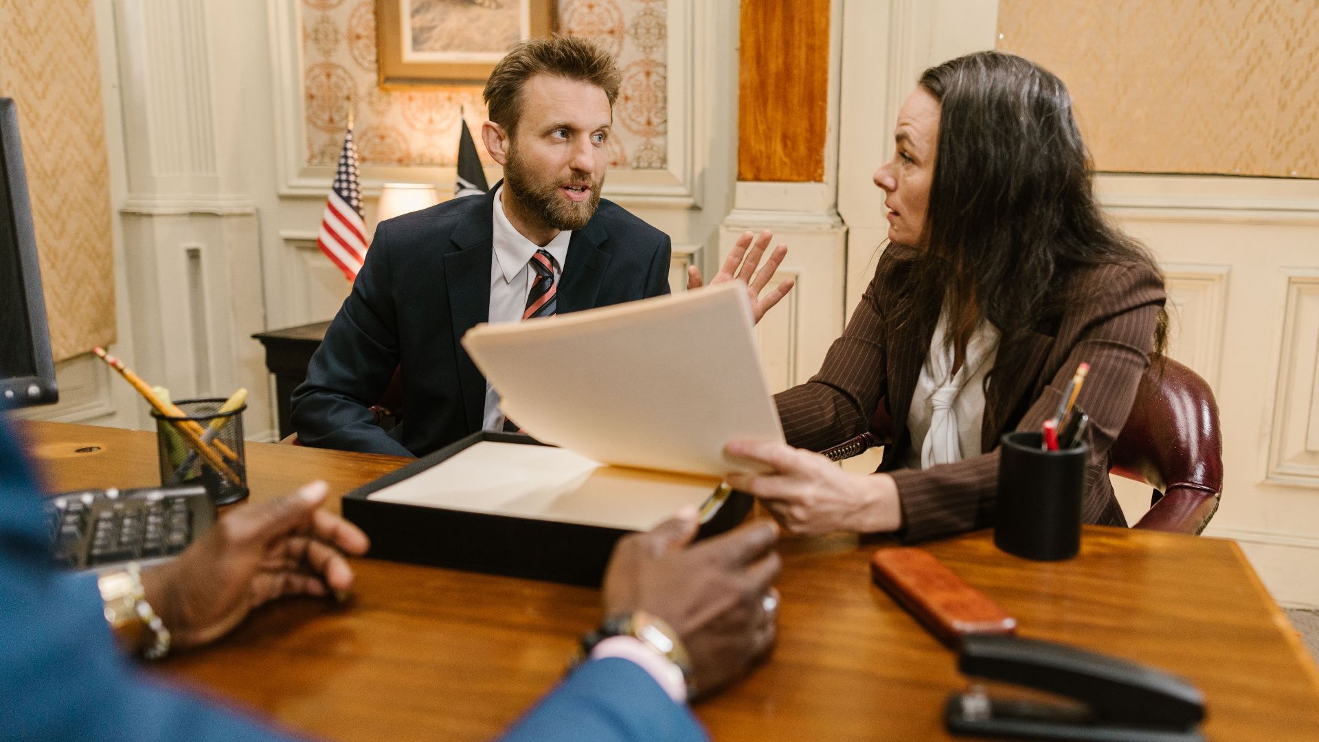 Diverse group in a corporate office engaged in a formal meeting. Professional attire and documents suggest a business discussion.