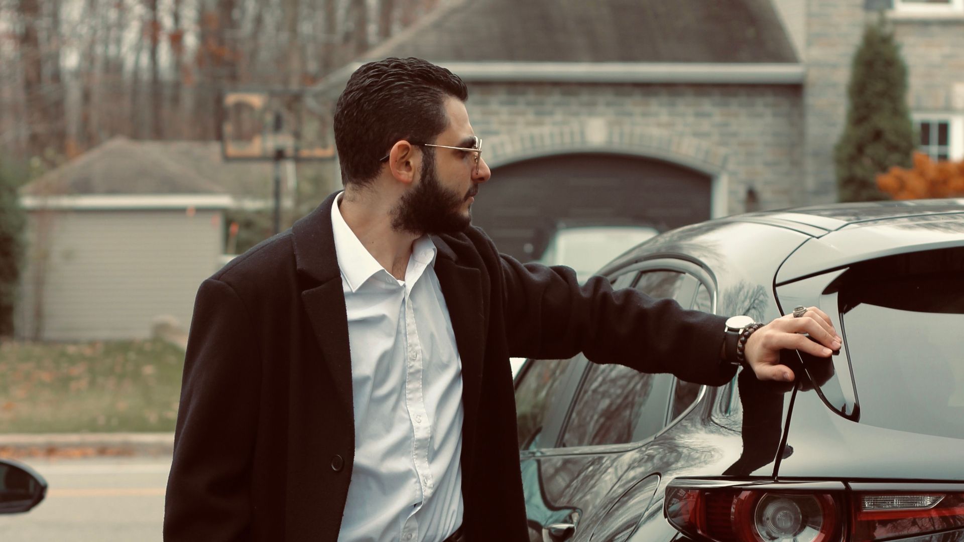 Fashionable man in a coat standing by his car in a suburban Canadian neighborhood.