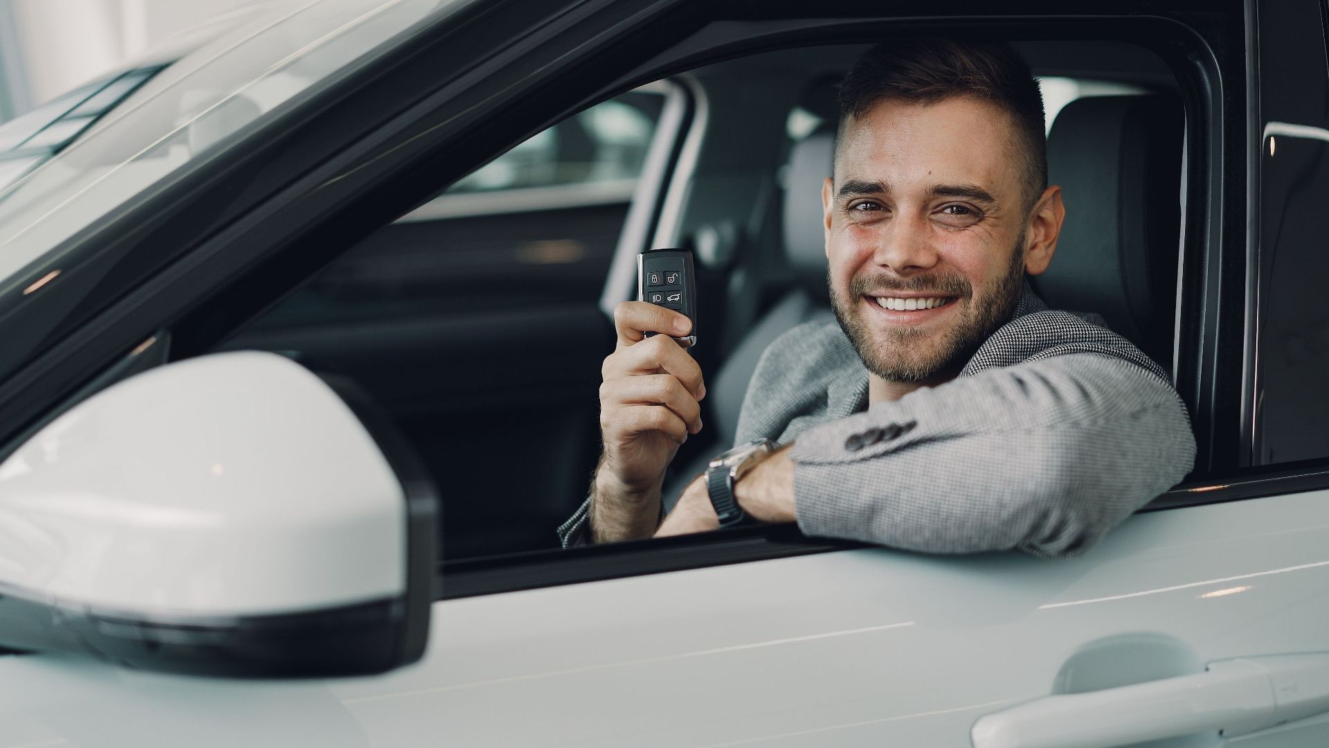 Happy young man holding car keys inside a vehicle. Perfect image for car rental or sales.