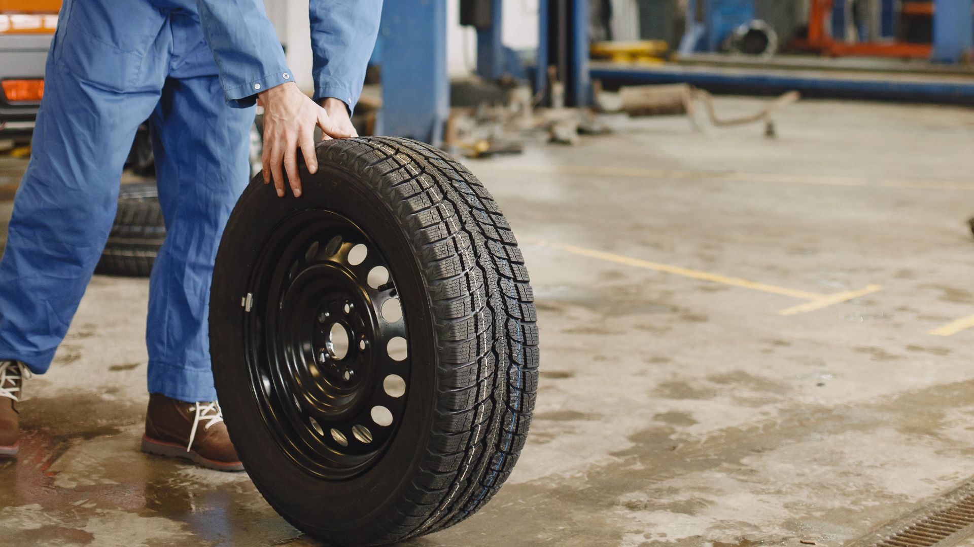 Mechanic handling a tire in a busy automotive repair workshop.
