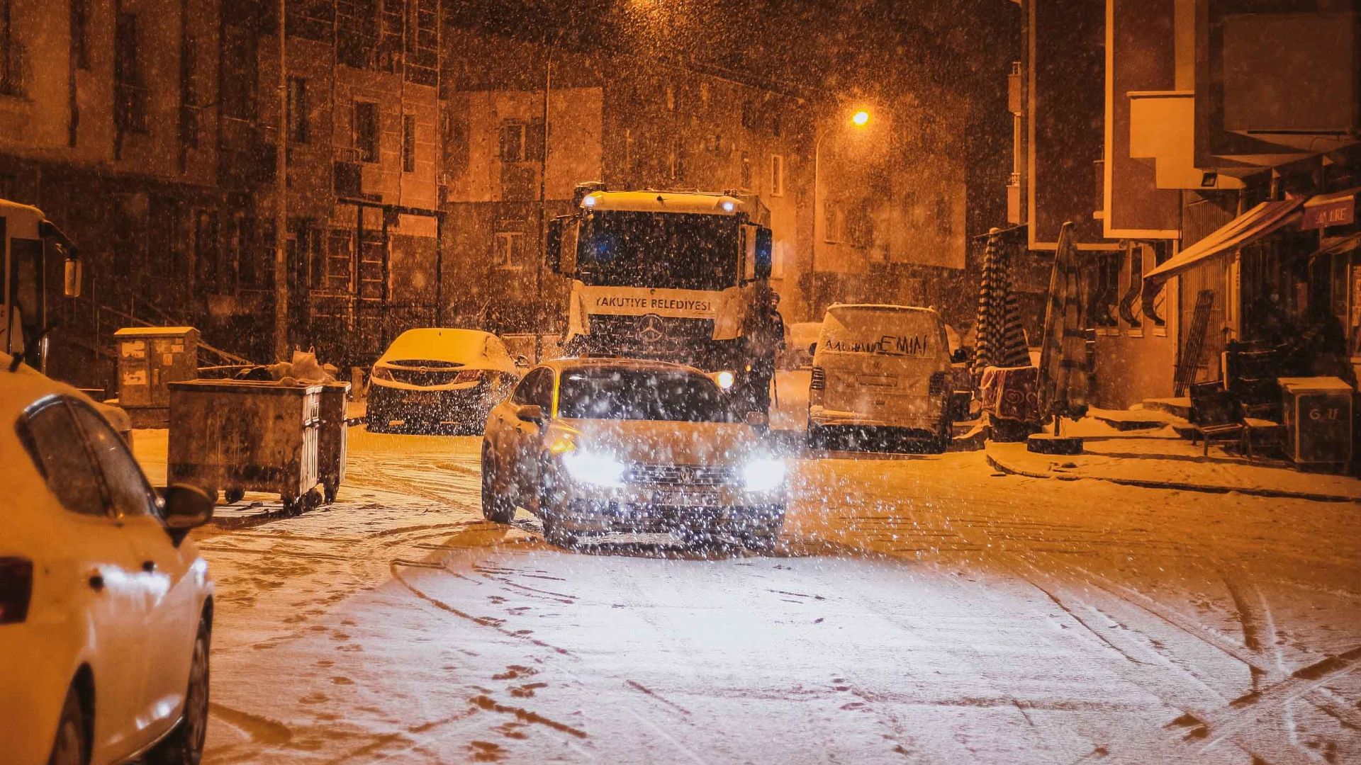 A serene winter night scene of snow-covered street with parked vehicles.