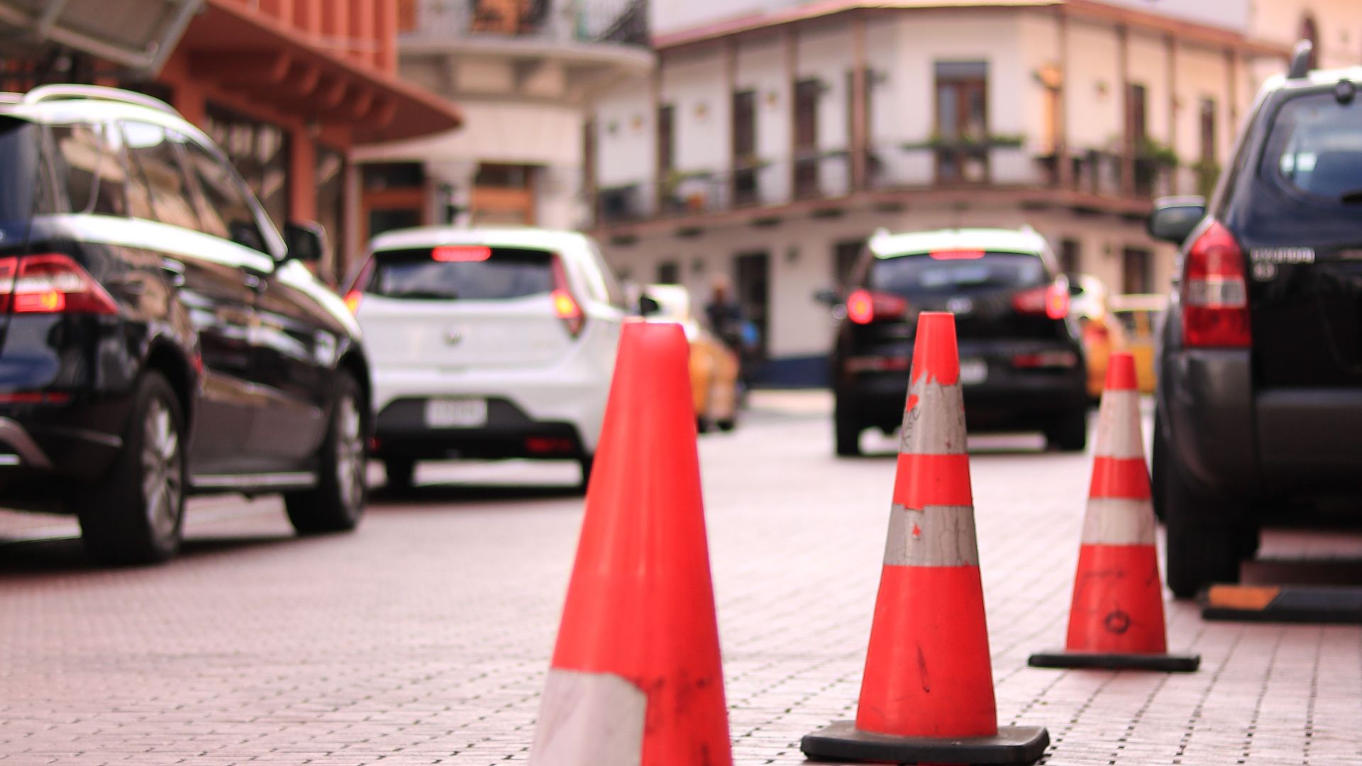Traffic cones line a cobblestone street in bustling Panama City, capturing urban life.