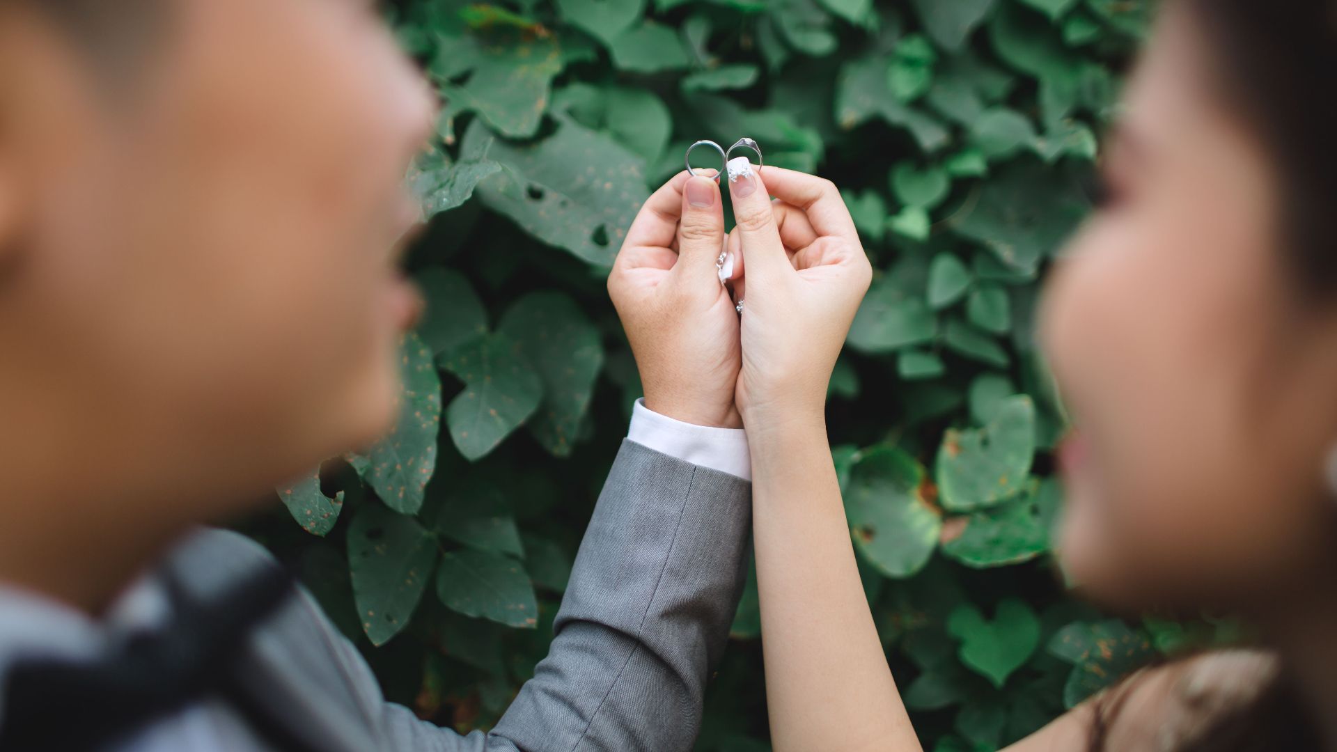 Close-up of a couple holding wedding rings with lush green background, symbolizing love and unity.