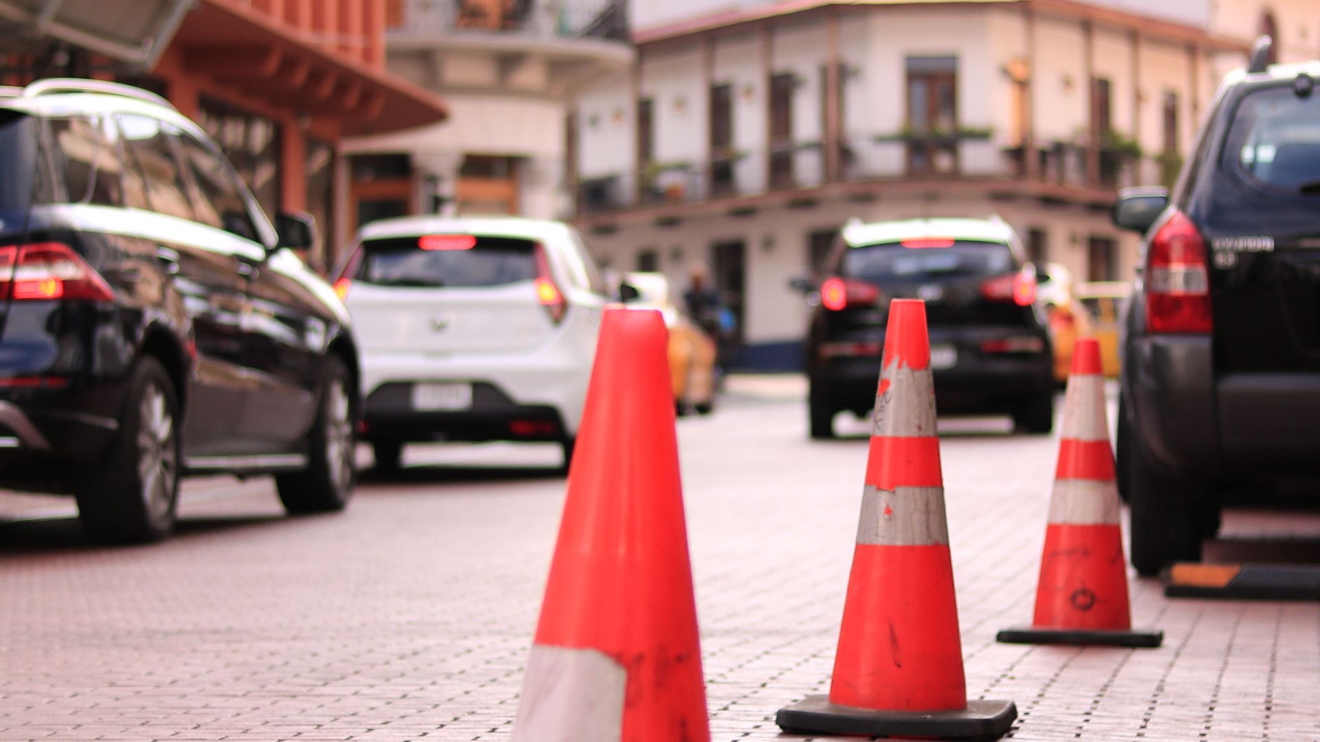 Traffic cones line a cobblestone street in bustling Panama City, capturing urban life.