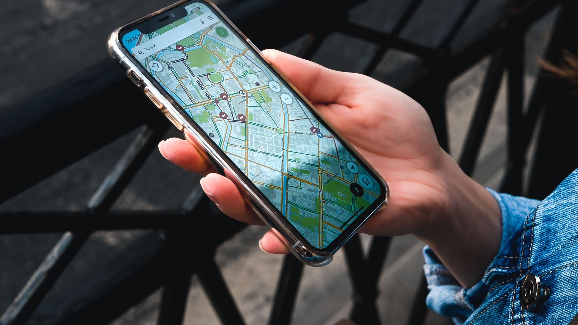 An outdoor close-up of a hand holding a smartphone displaying a map application.