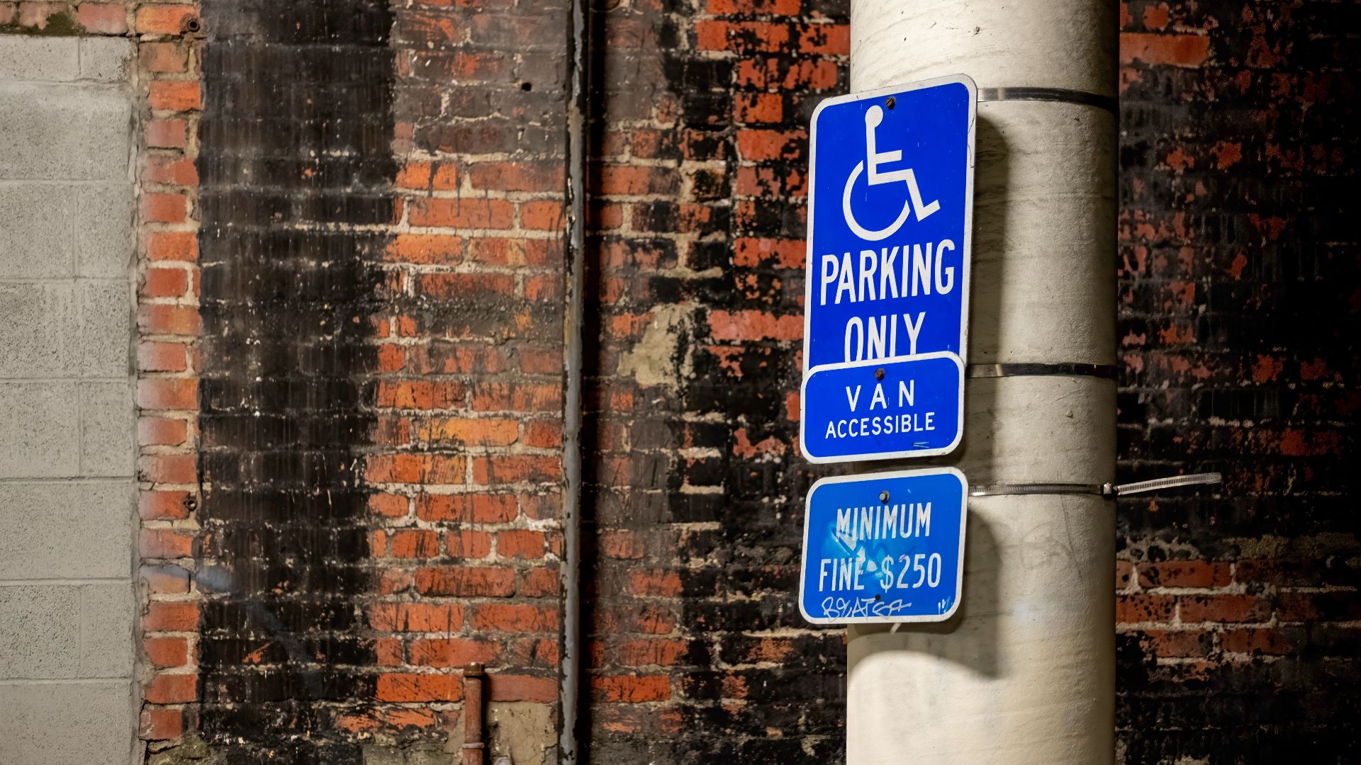 Blue handicap parking sign attached to a pole against a brick wall in the city.