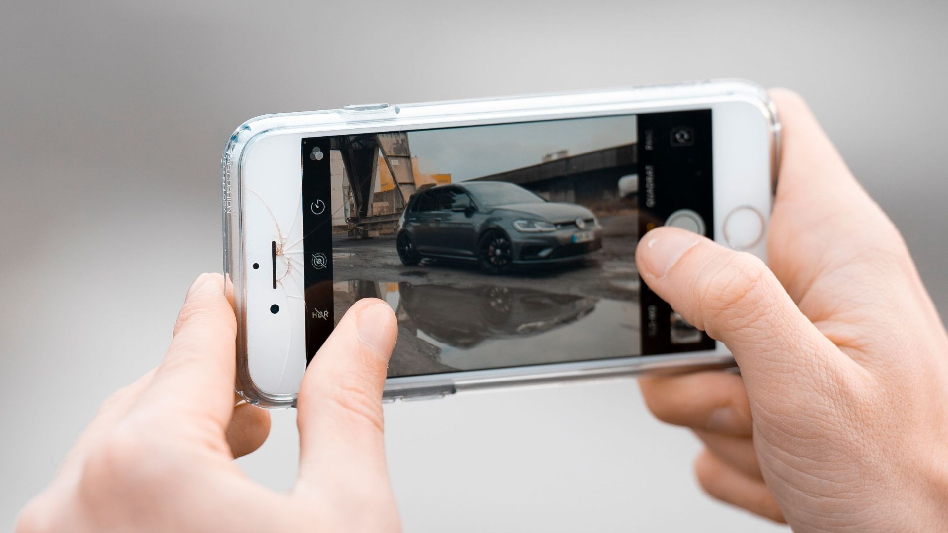 Close-up of hands photographing a car with a smartphone outdoors.