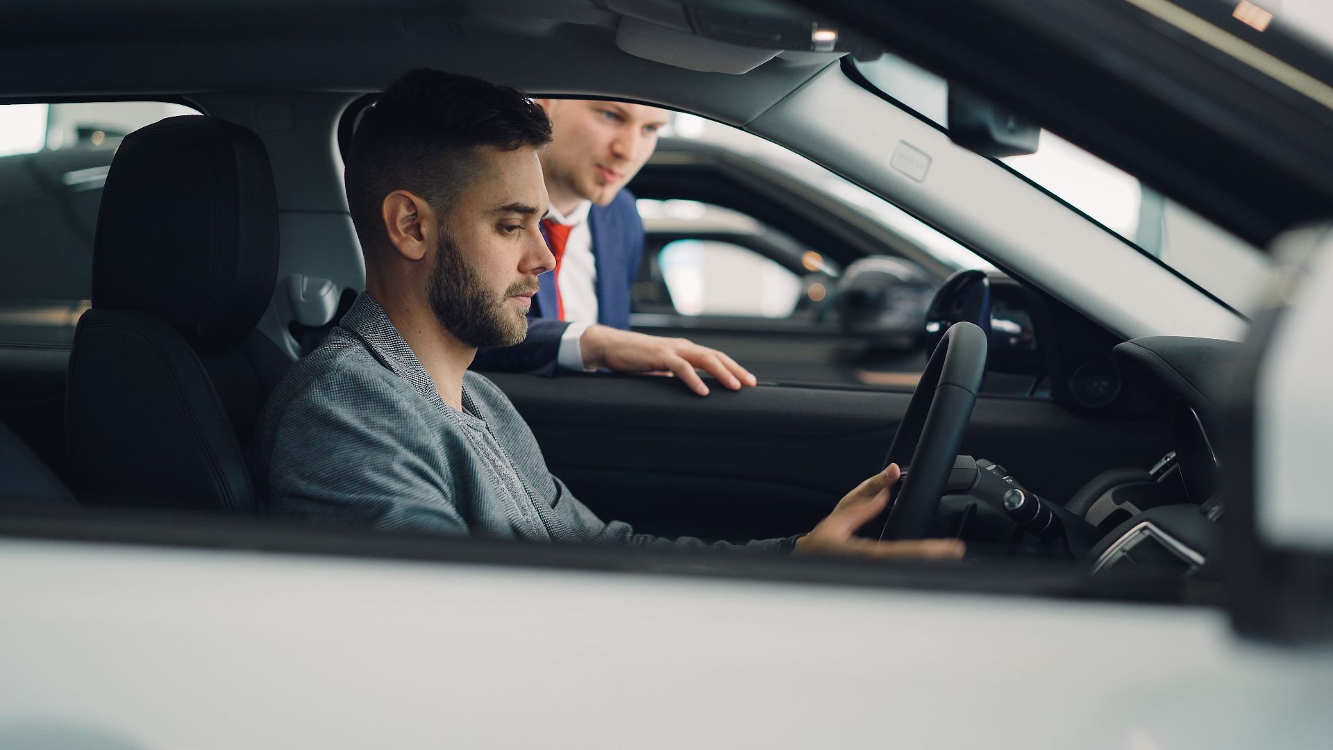 Man examining car interior with salesman at a dealership, highlighting car features.