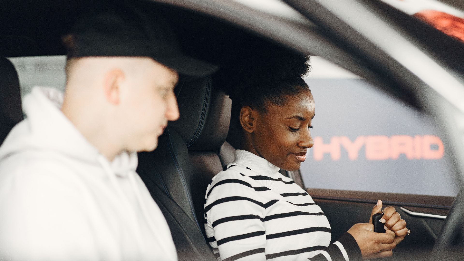 A man and woman sitting inside a hybrid car, discussing its features, highlighting modern eco-friendly transportation.