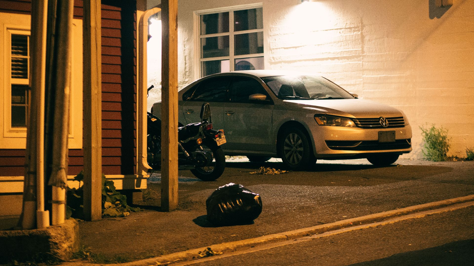 Volkswagen car and motorcycle parked in a dimly lit urban area at night.