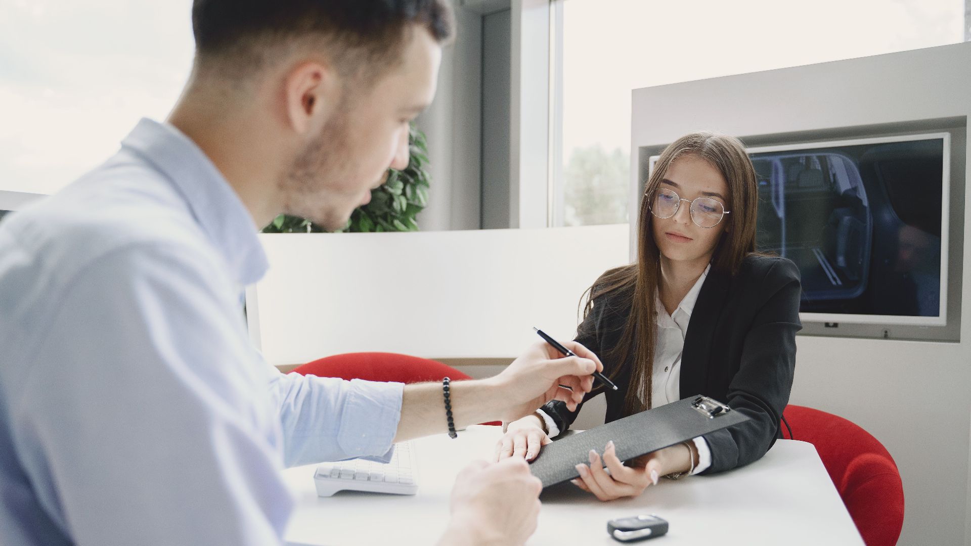 A man and woman discussing and signing a document at a table in an office setting.