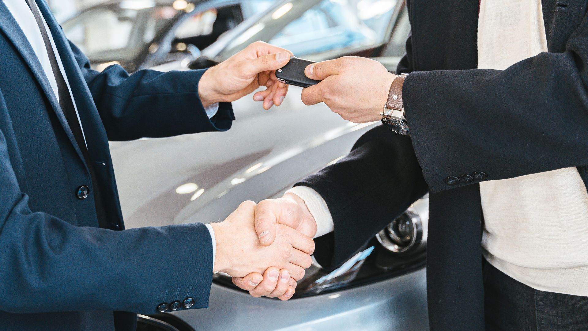 Two businessmen shaking hands and exchanging car keys in a dealership. Symbolizes a successful deal.