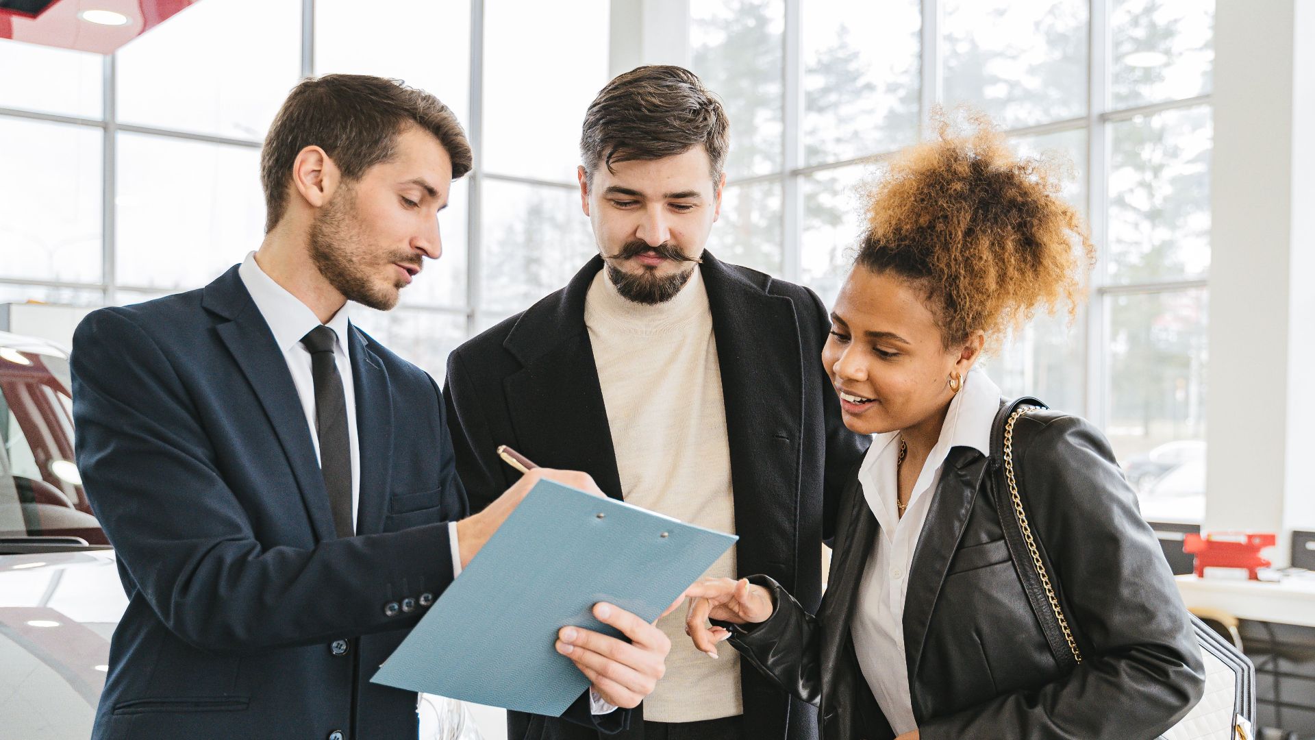 Three business professionals discussing car purchase details inside a modern dealership.