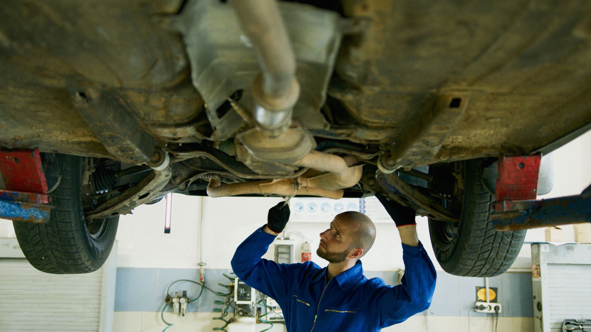 Mechanic examining the underside of a car in an auto repair shop for maintenance.