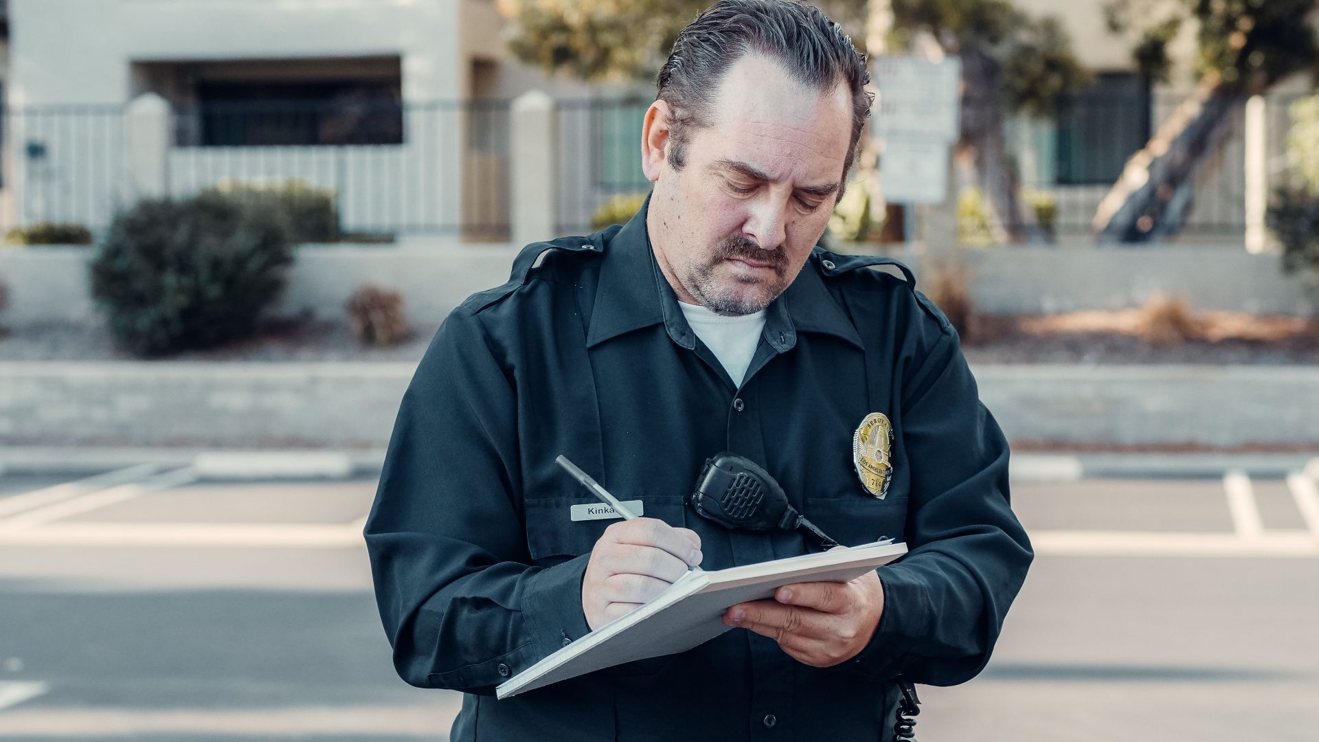 Police officer in uniform writing a ticket on a clipboard outdoors.