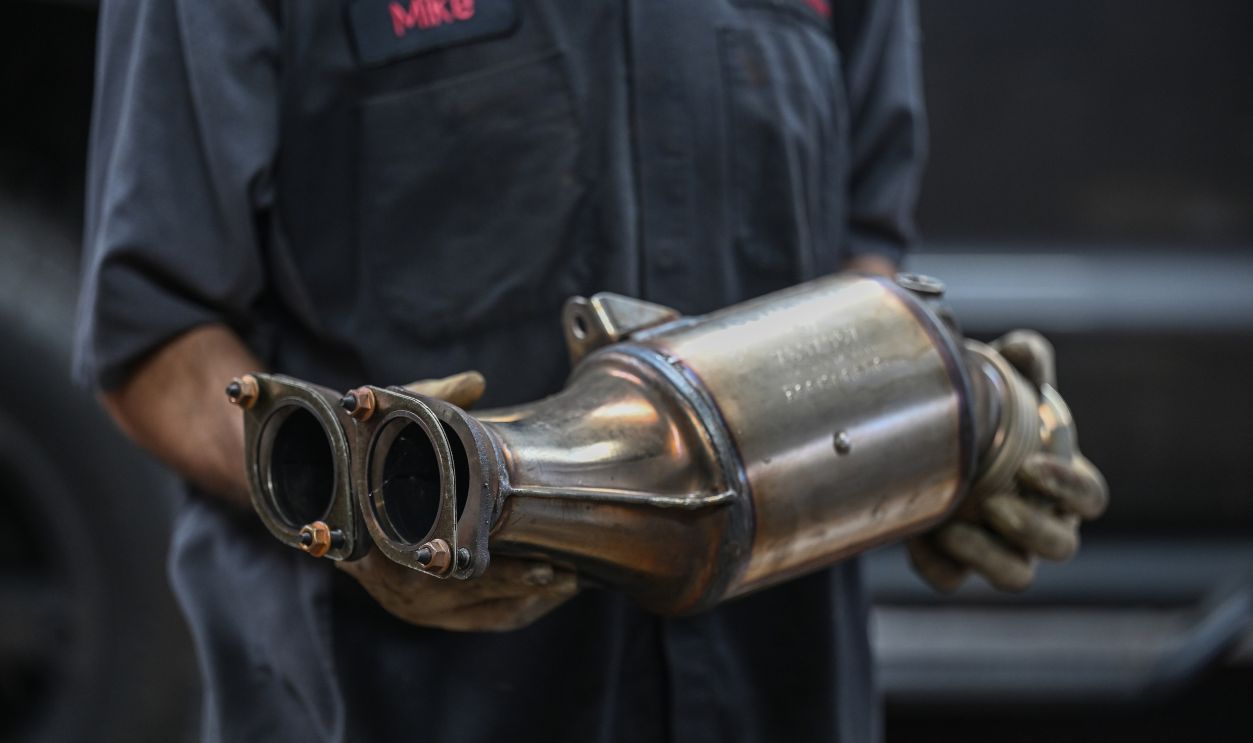 auto mechanic holding catalytic converter in auto repair shop
