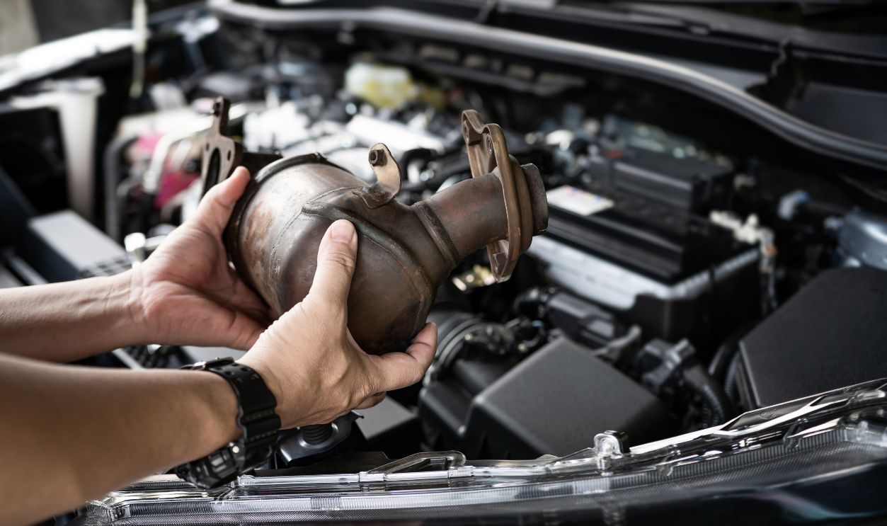 Close up old catalytic converter in hand Car service staff remove from engine gasoline car dust clogged condition on filter in service concept and engine room in the background