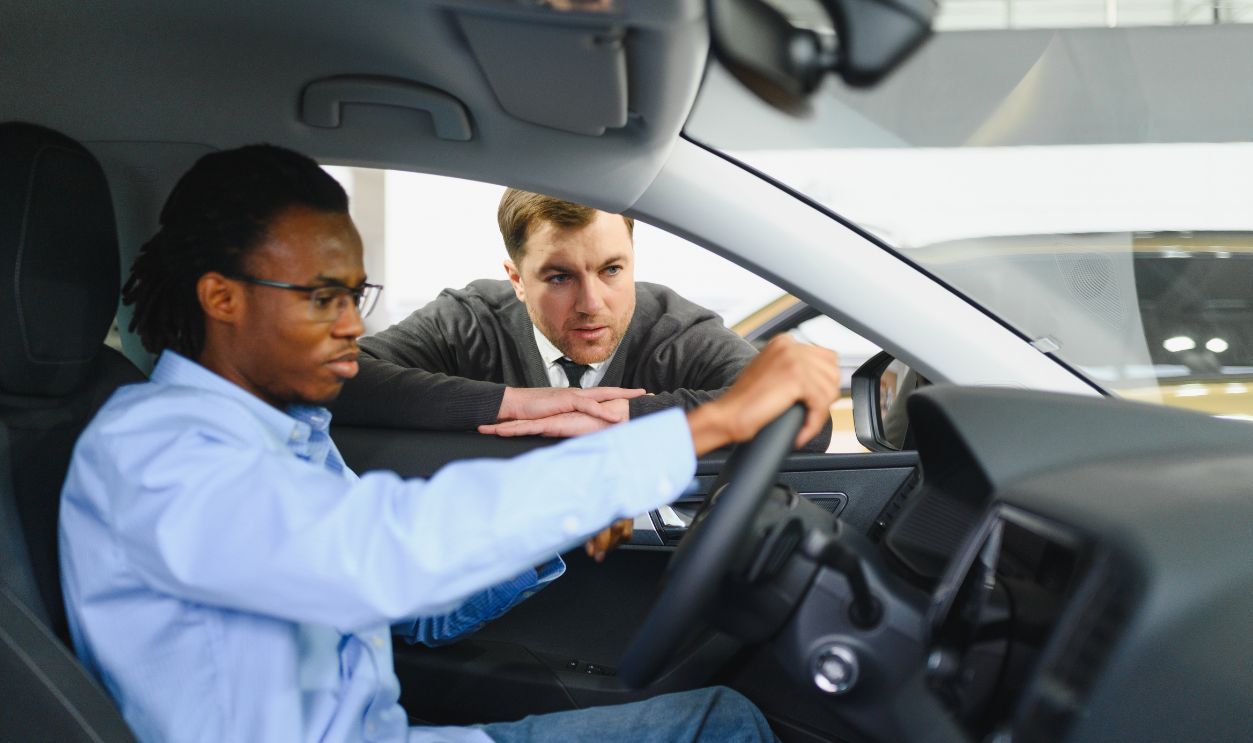 Shutterstock - 2683893331 - Male car dealer having conversation with pensive young man client at showroom. Man listening manager while buying car at dealership center.