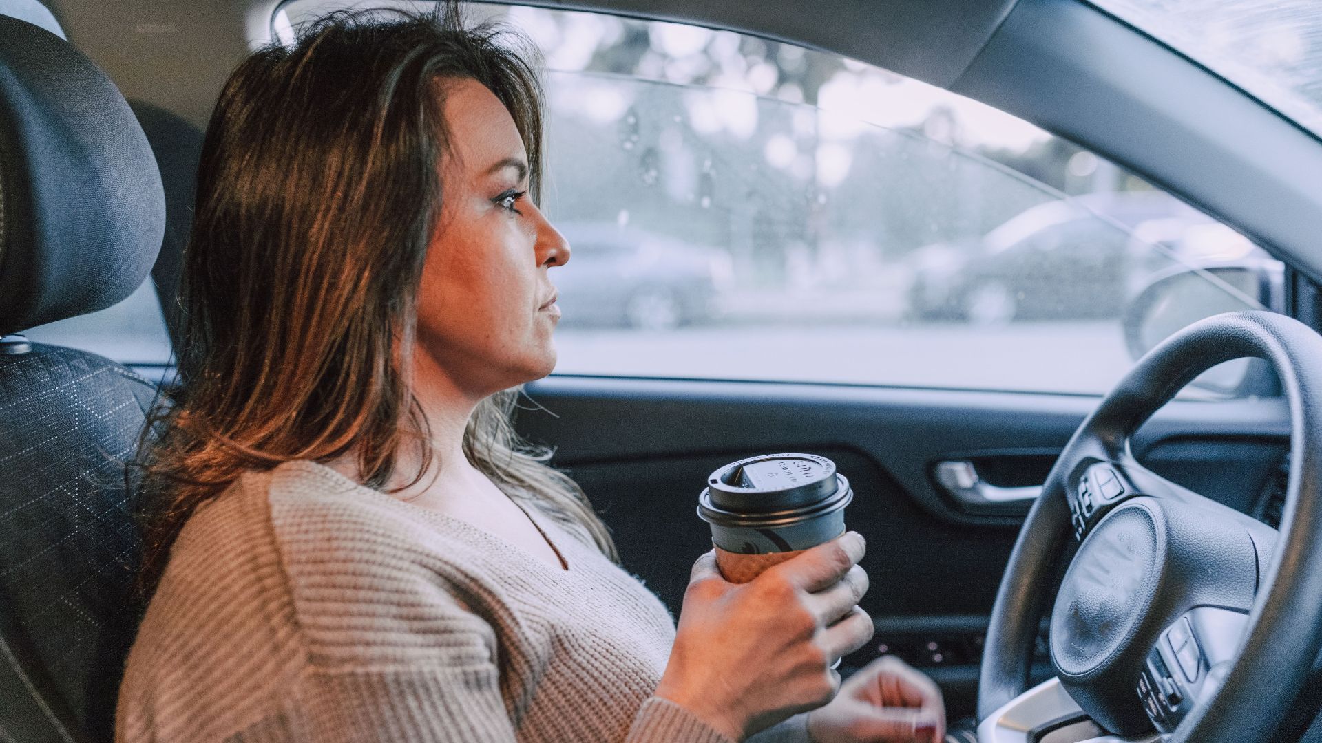 A woman in a car holding a disposable coffee cup, showing focus.
